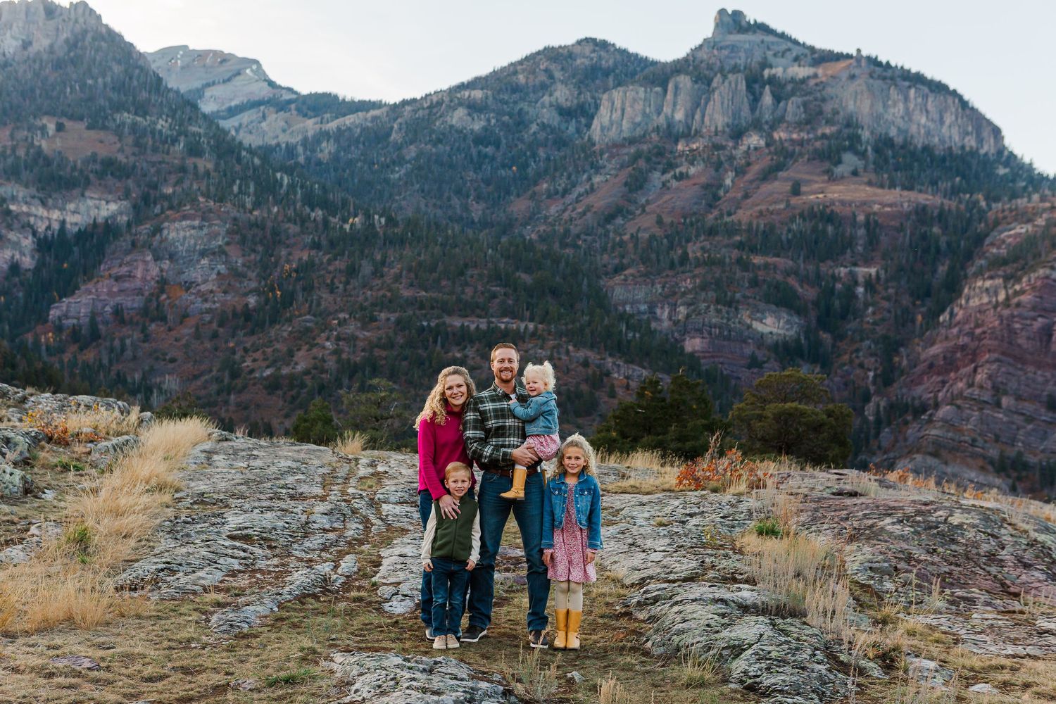 Family group poses together on rocky mountain trail with dramatic peaks in background.