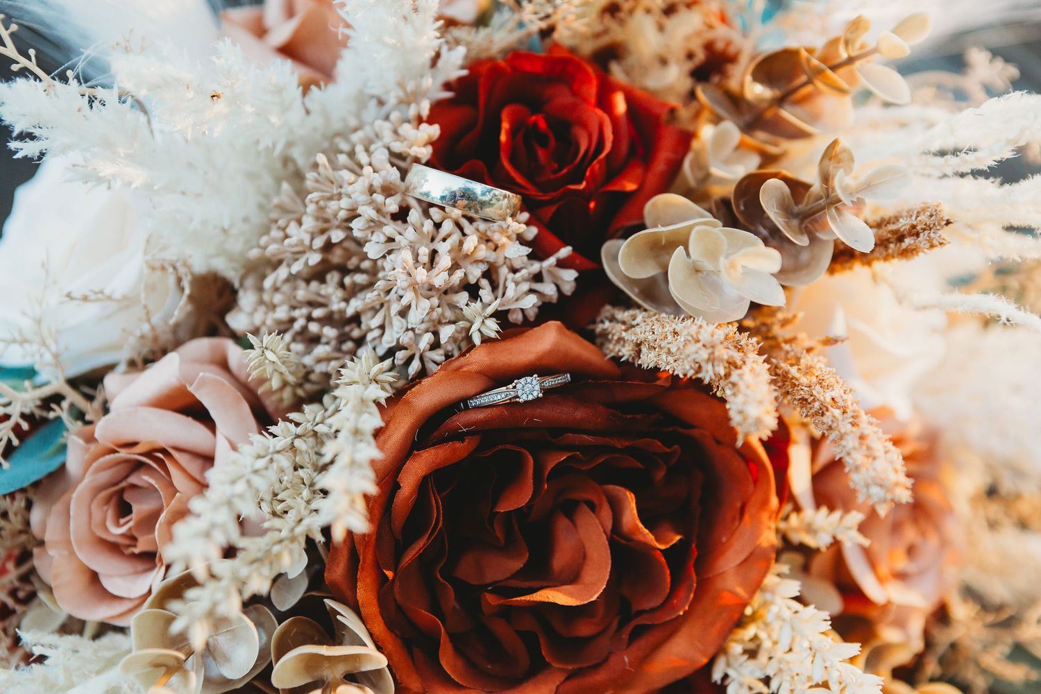 Close-up of luxurious wedding bouquet featuring deep red and pink roses with dried elements.