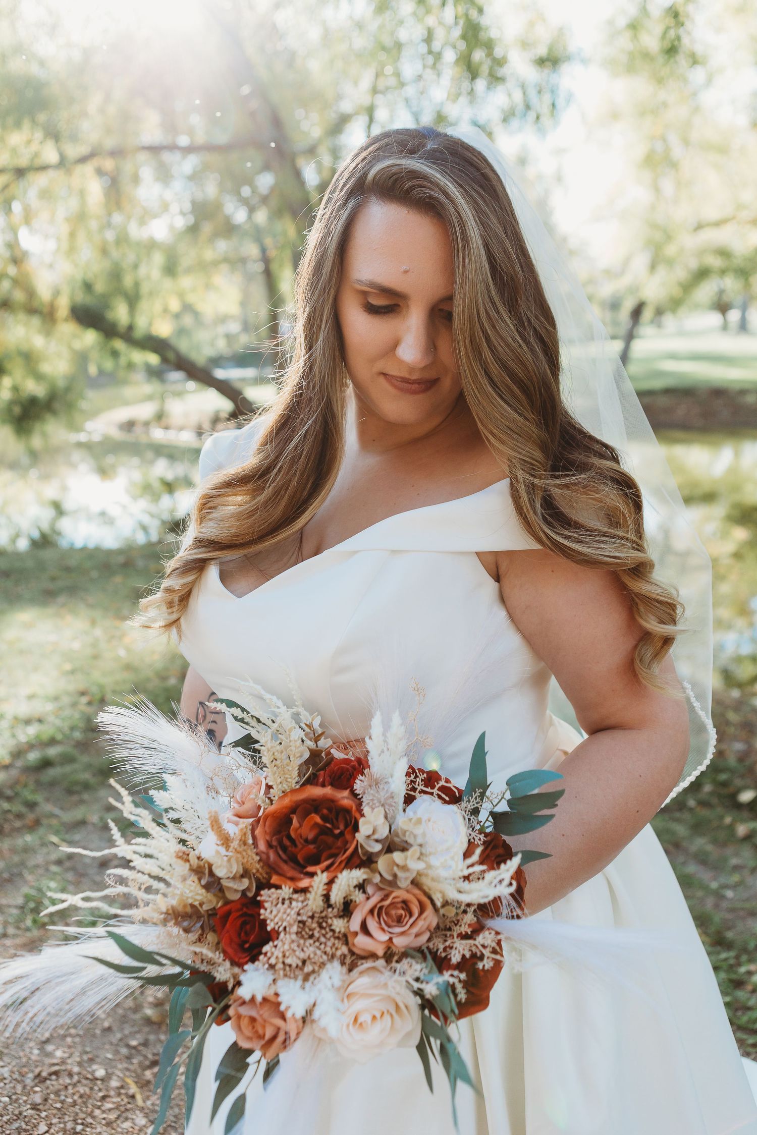 A bride in a white wedding dress holds a stunning autumn-toned bouquet with pampas grass and roses.