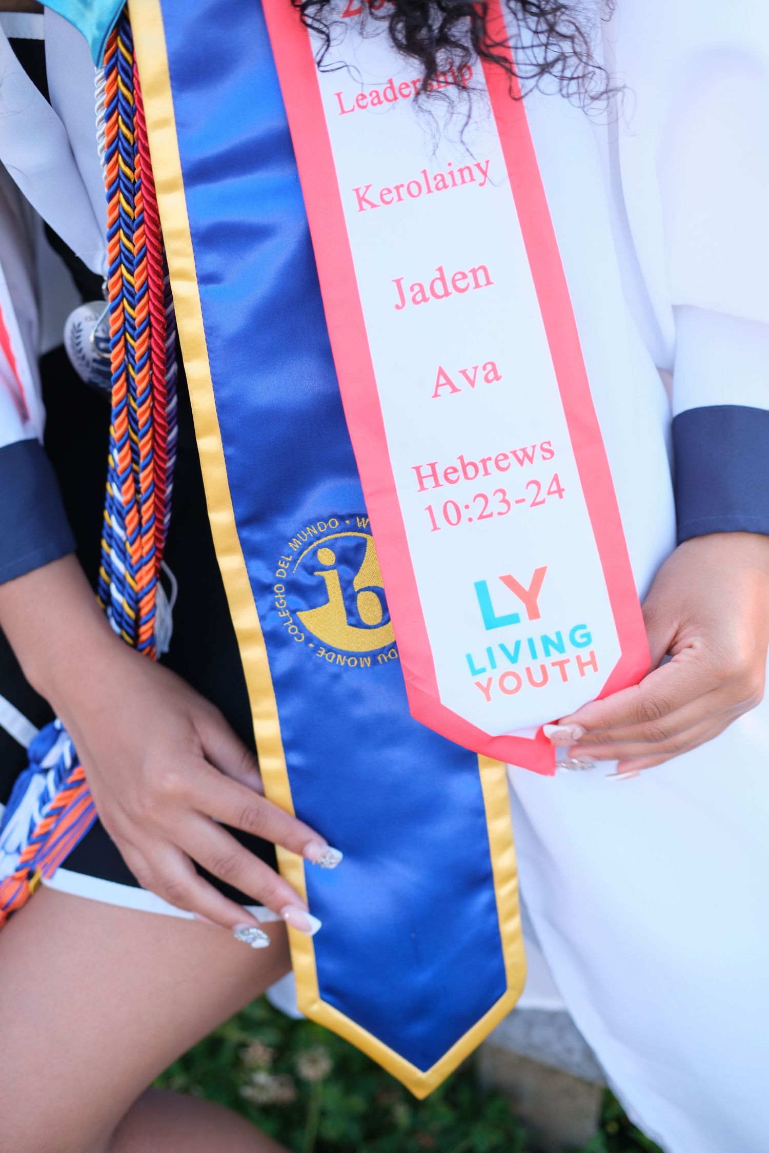 Graduation stole with names Kerolainy, Jaden, Ava, Hebrews 10:23-24, and Living Youth logo on blue sash.