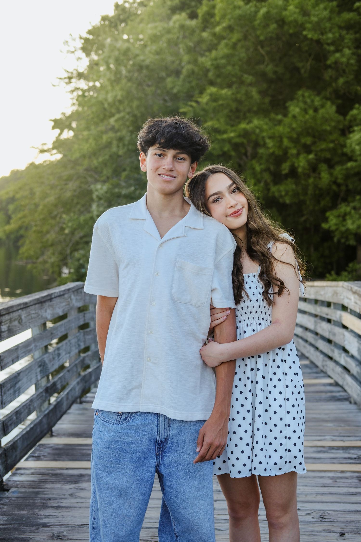 Young teenage couple poses together on a wooden bridge at golden hour sunset.