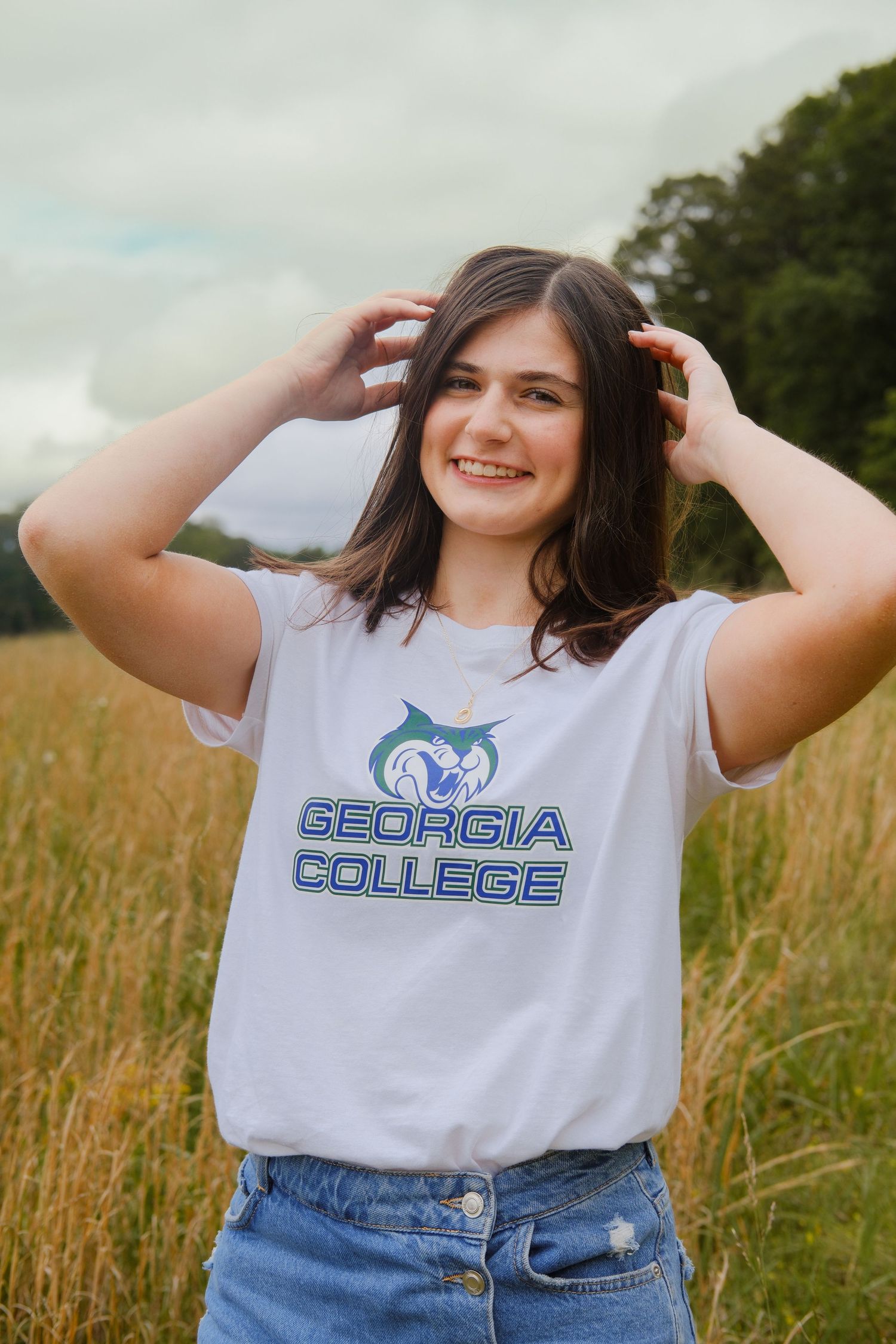 Smiling young woman in Georgia College t-shirt posing in a golden wheat field.