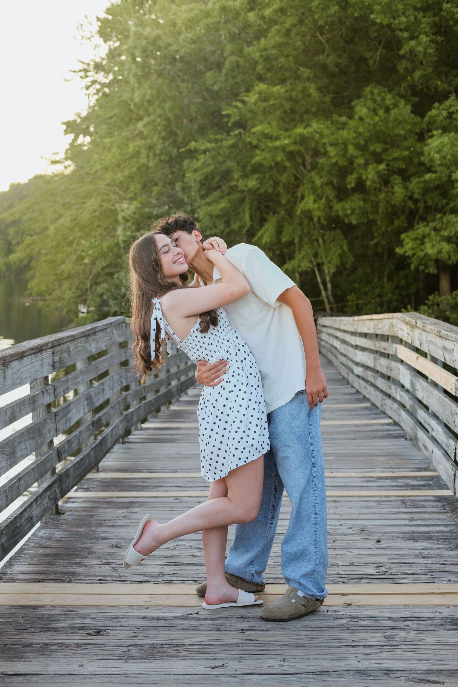 Young couple shares a romantic kiss while embracing on a wooden bridge at sunset.