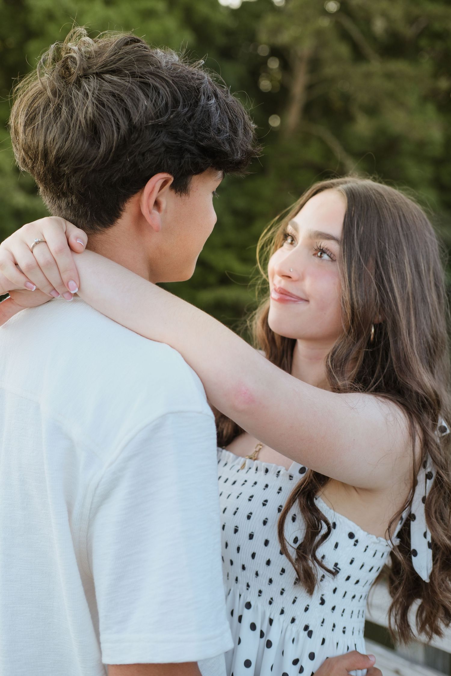 Young woman smiles warmly while embracing her boyfriend outdoors in soft natural light.