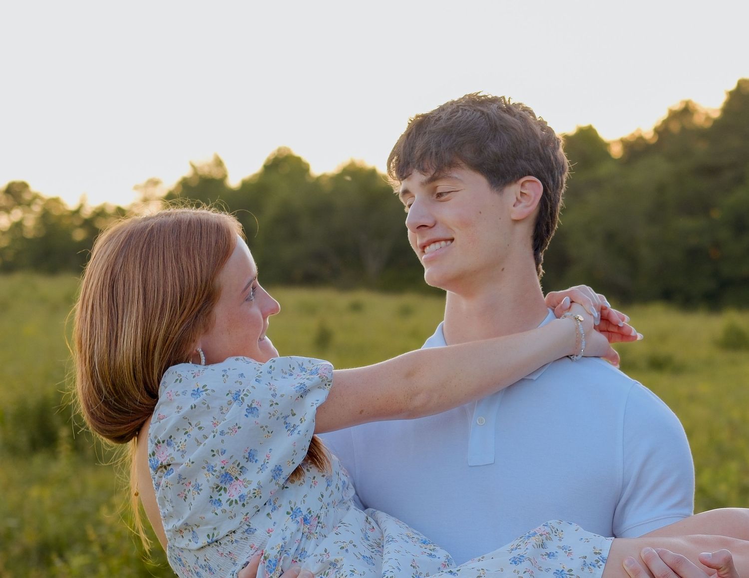 Young couple sharing a romantic moment in a sunny green field, woman in floral dress embracing smiling man.