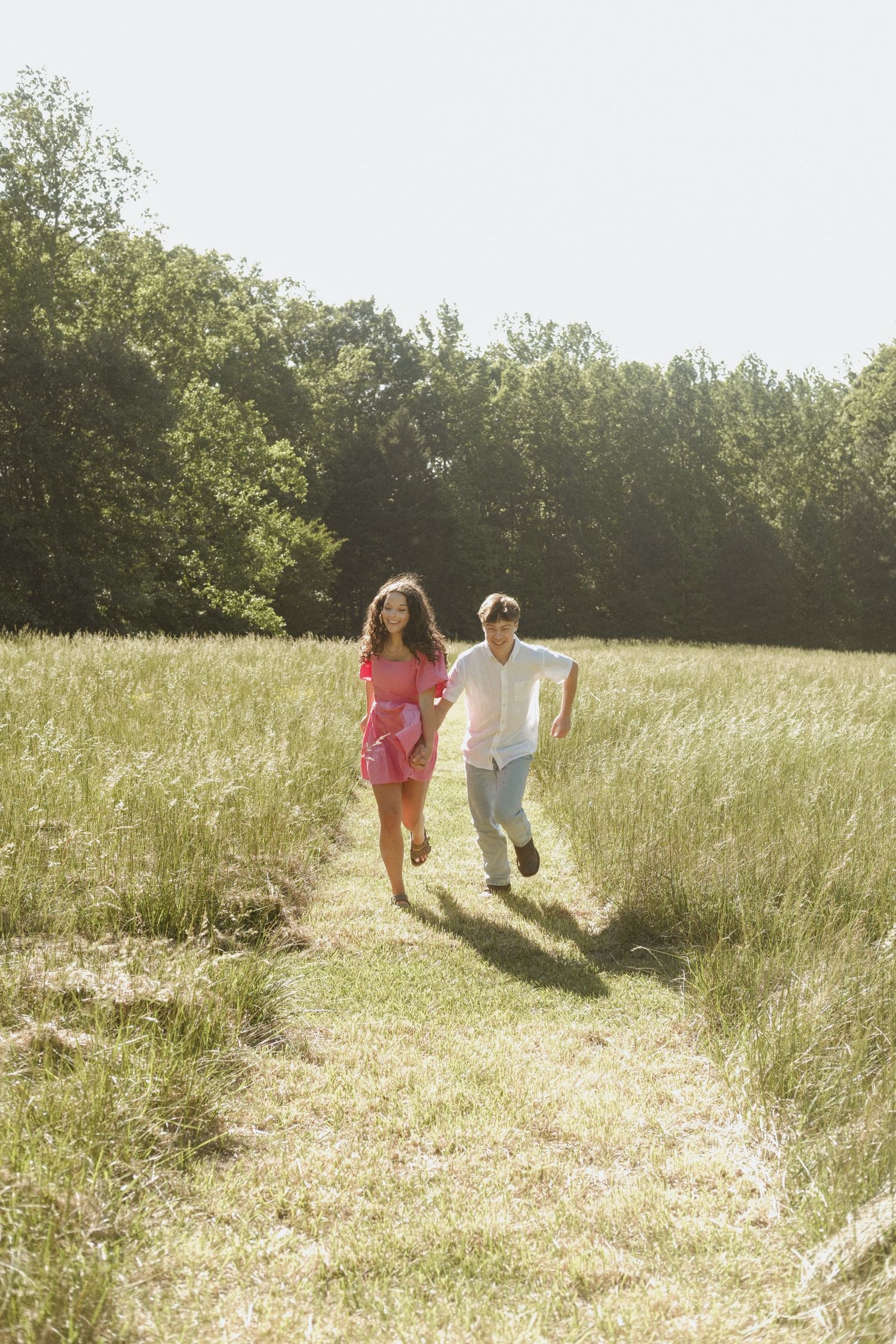 Happy couple running hand in hand along a grassy field path on a bright sunny day.