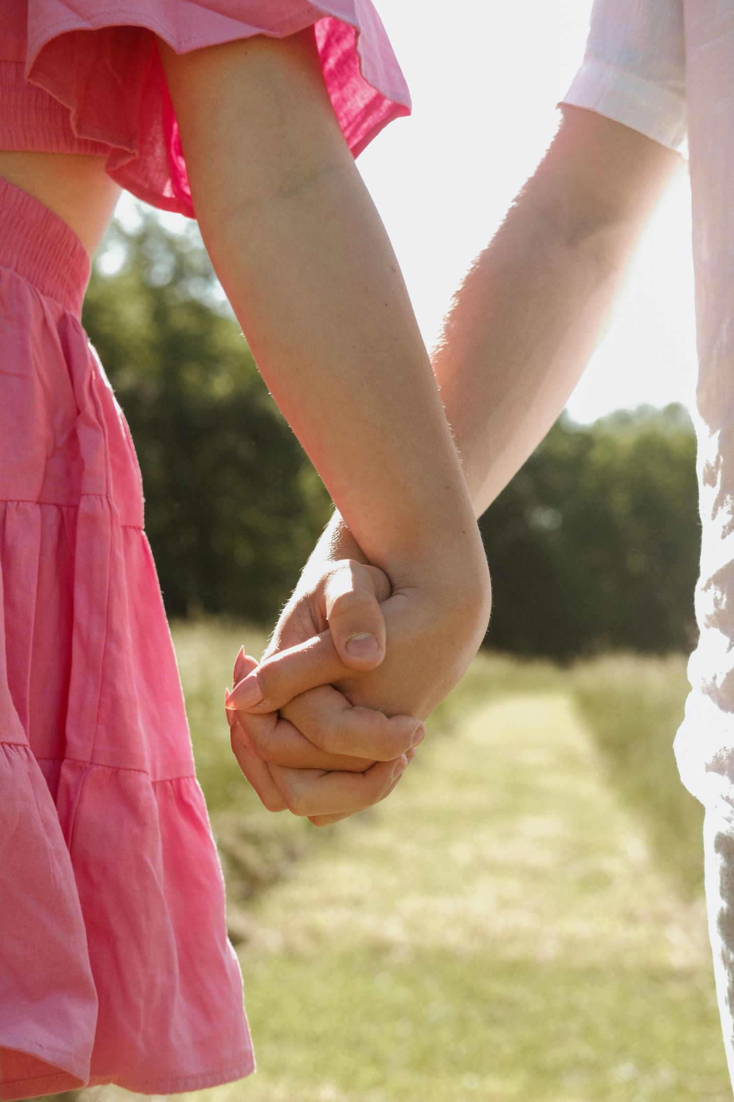 Close-up of a couple holding hands in a sunny field, woman wearing a pink dress, symbolizing love and togetherness.