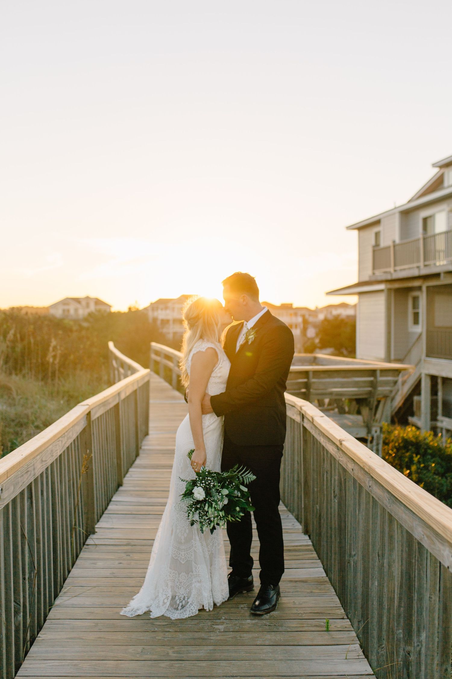 Sunset wedding portraits on wooden boardwalk with coastal homes in background.