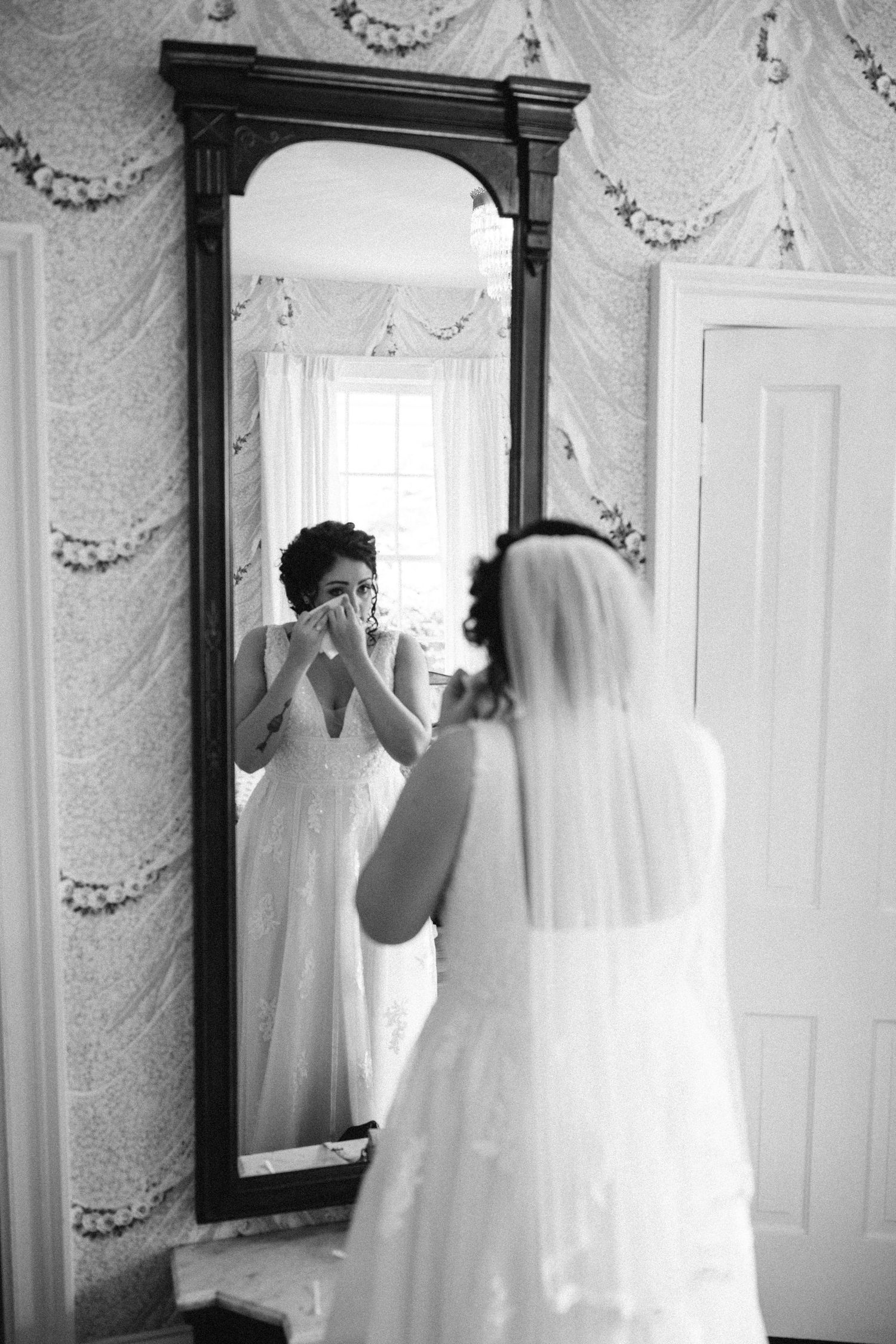 Black and white photo of a wedding dress displayed in a room with ornate mirrors and decorative wall moldings.