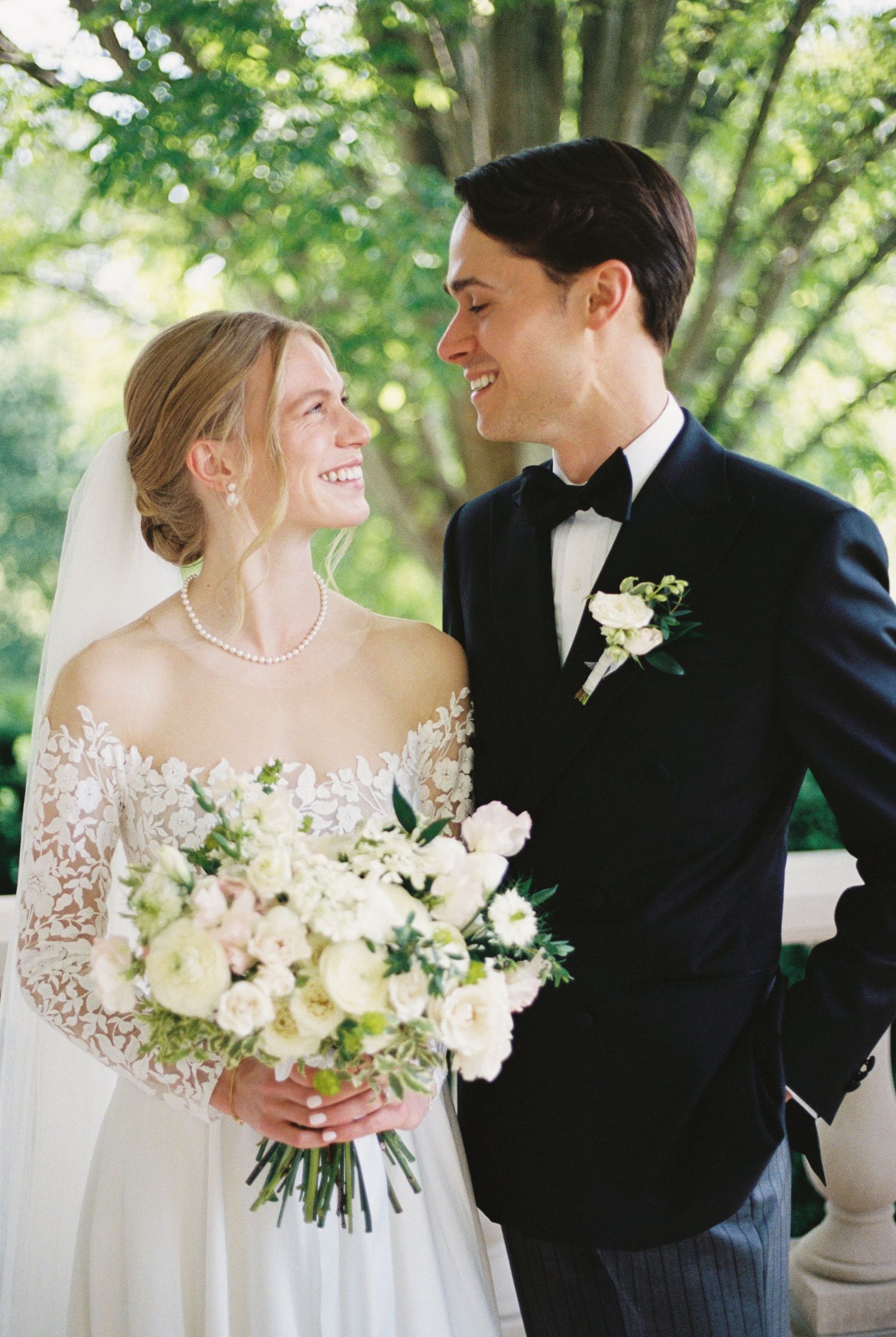 A couple shares romantic moments in their wedding attire holding white floral bouquets.