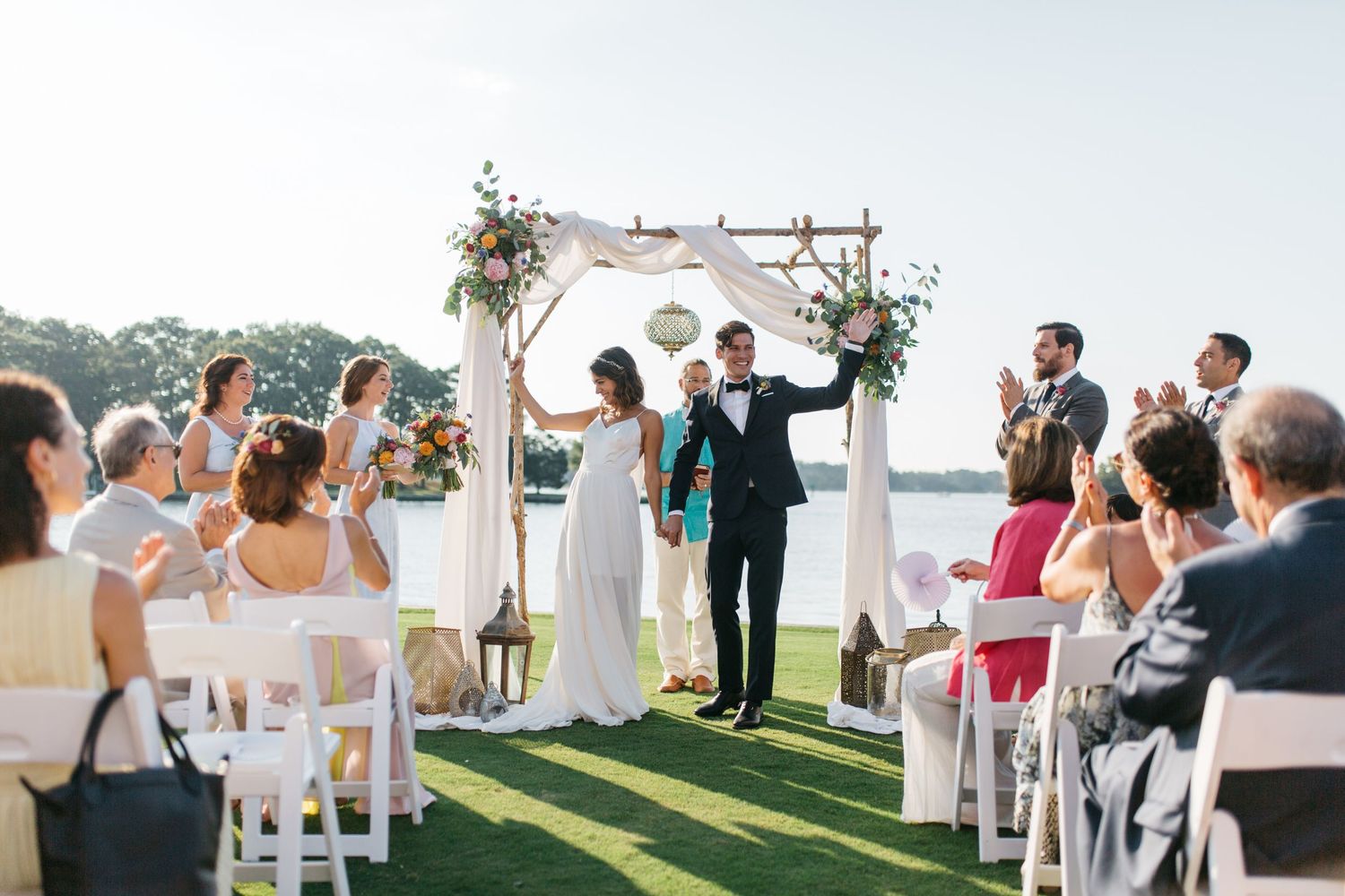 White chairs set up for outdoor wedding ceremony with guests seated.