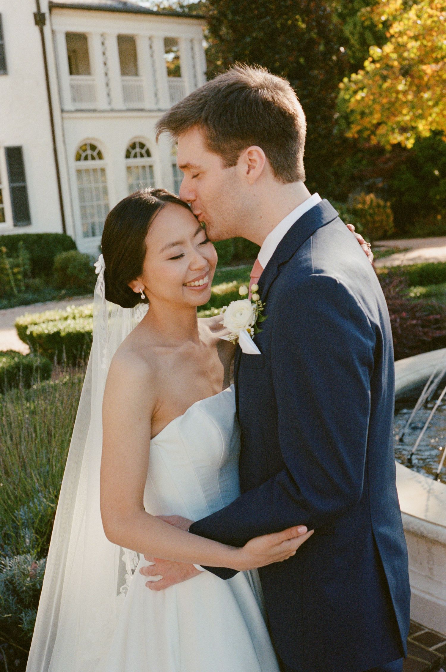 Romantic wedding couple embraces in golden sunlight against a classic building backdrop.