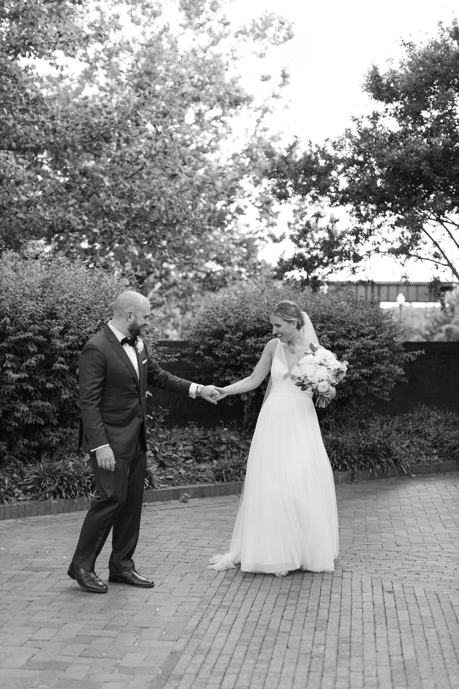 Wedding couple dances on brick pathway surrounded by greenery.