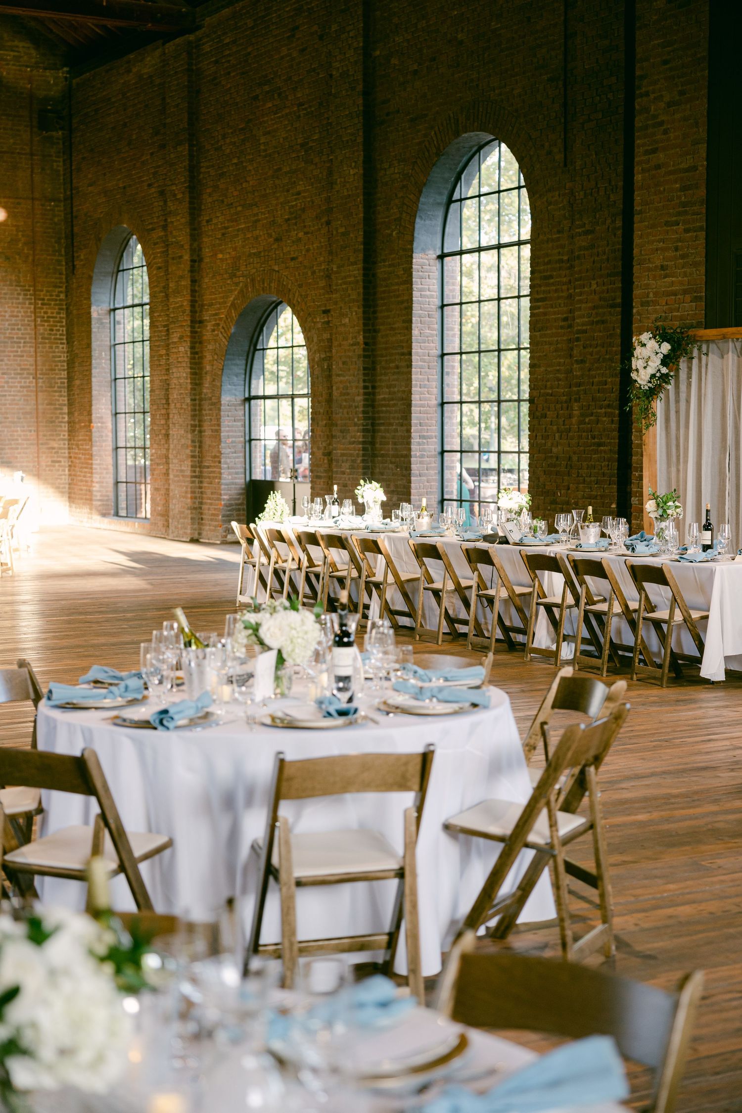 An elegant wedding reception venue with arched windows and round tables set for dinner.