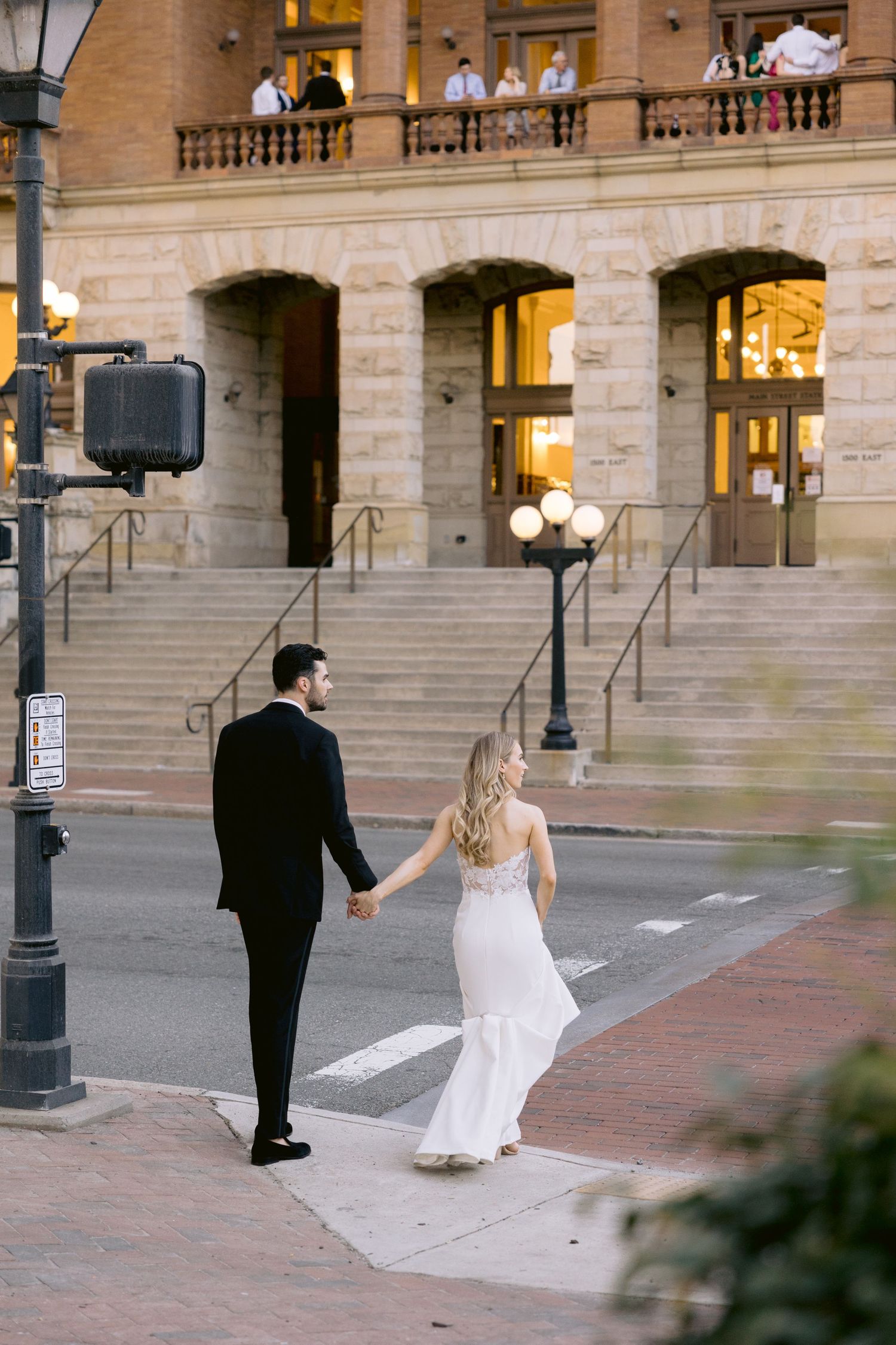 Wedding couple taking selfies on historic building steps at dusk.