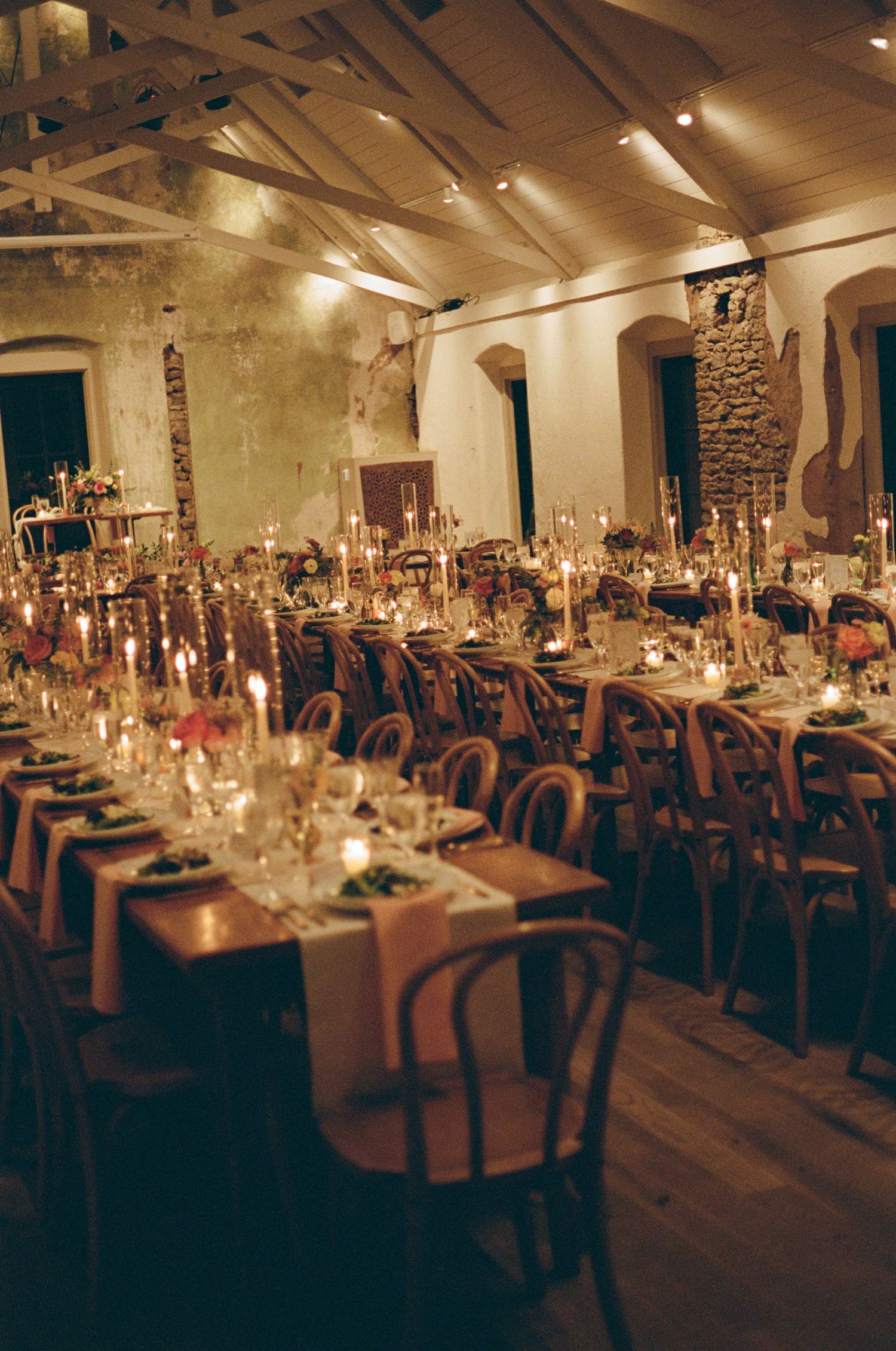 Elegant wedding reception venue with long tables set with glowing candles and formal place settings.