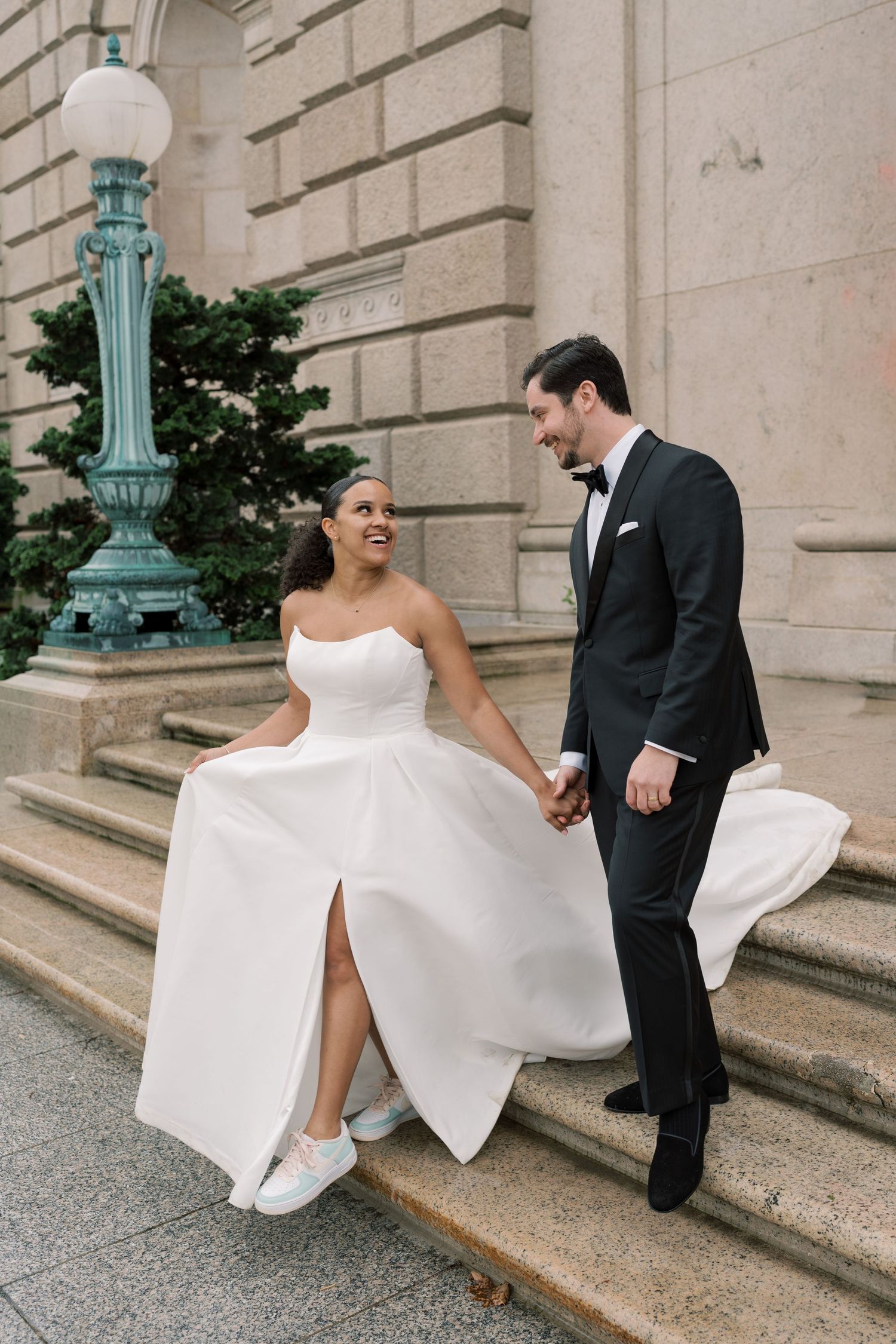 Playful wedding couple interacts on grand stone steps of historic building.