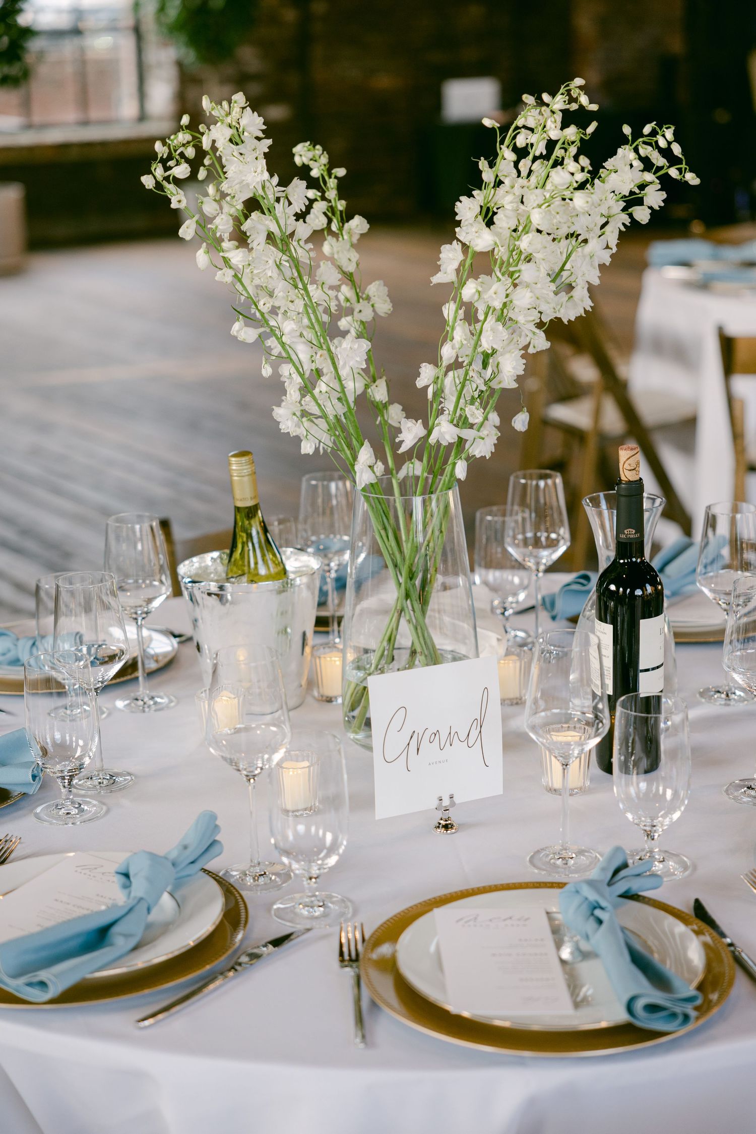 Elegant wedding table settings with white flowers, blue napkins, and gold charger plates.
