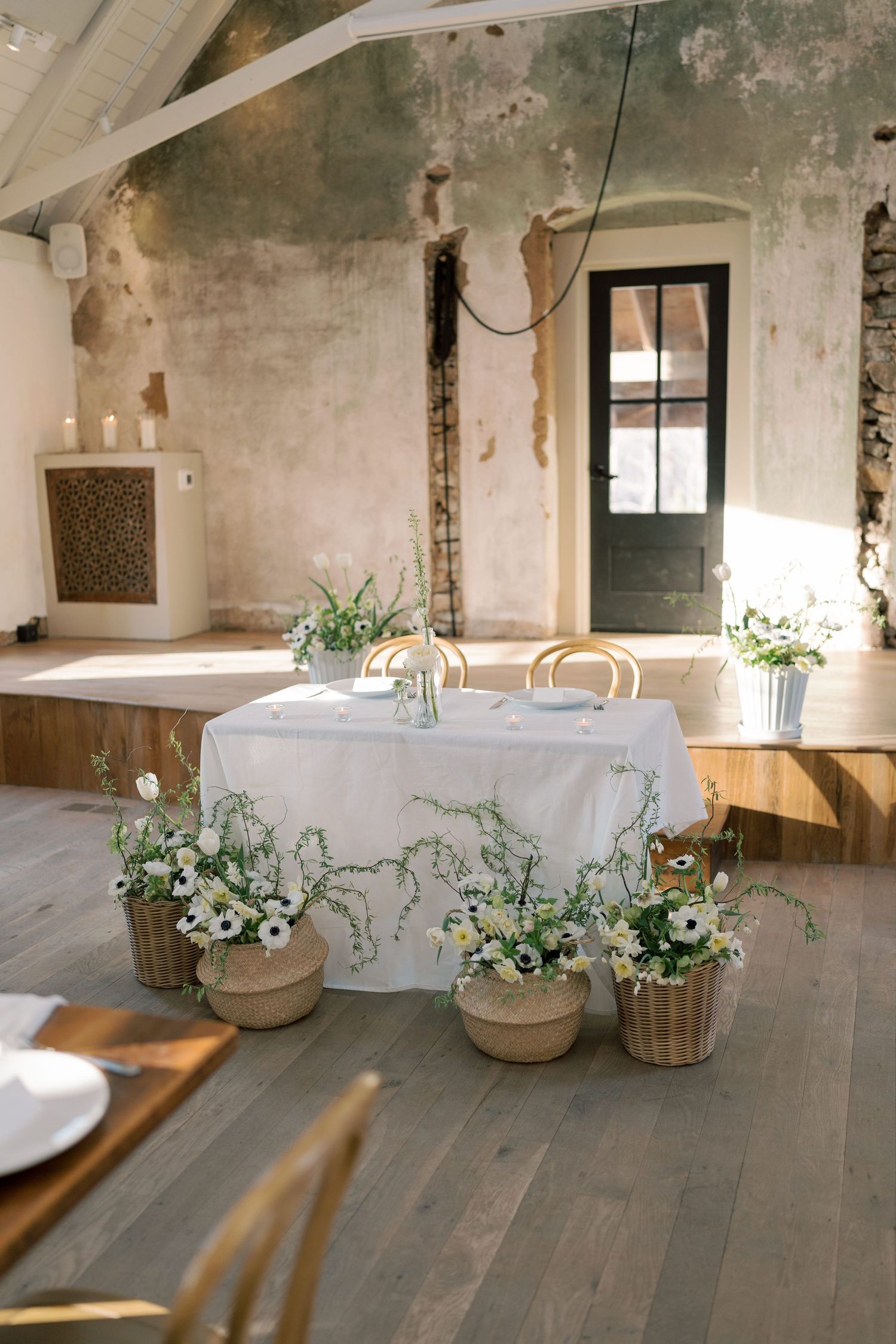 Rustic wedding reception space with white floral arrangements in wooden baskets.