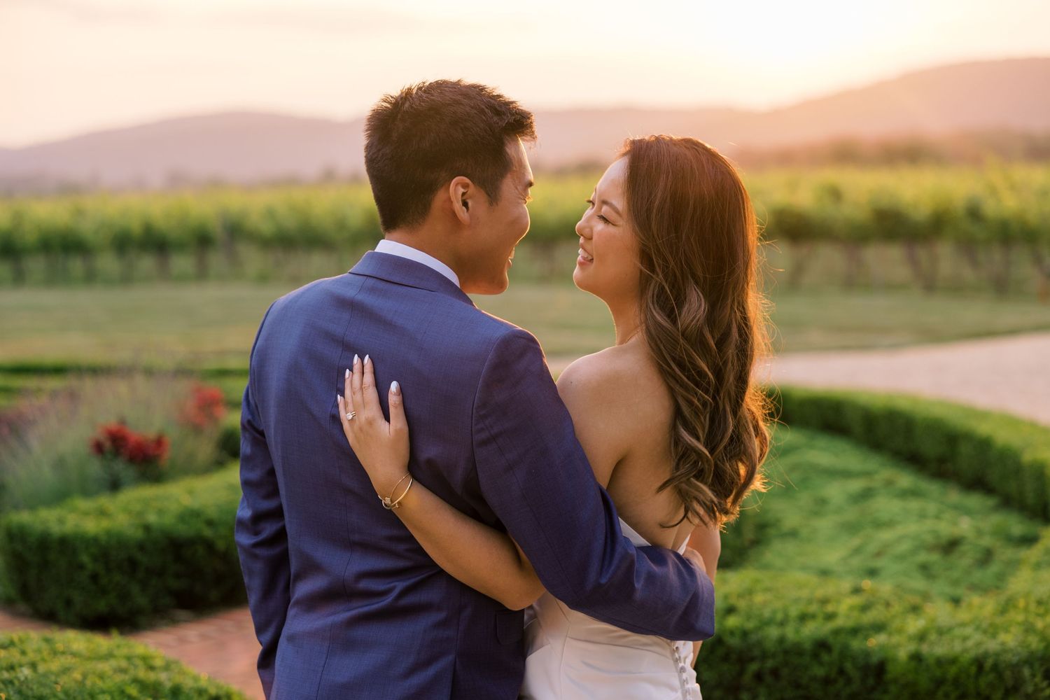 Couple embraces in golden sunlit field during outdoor wedding photoshoot.