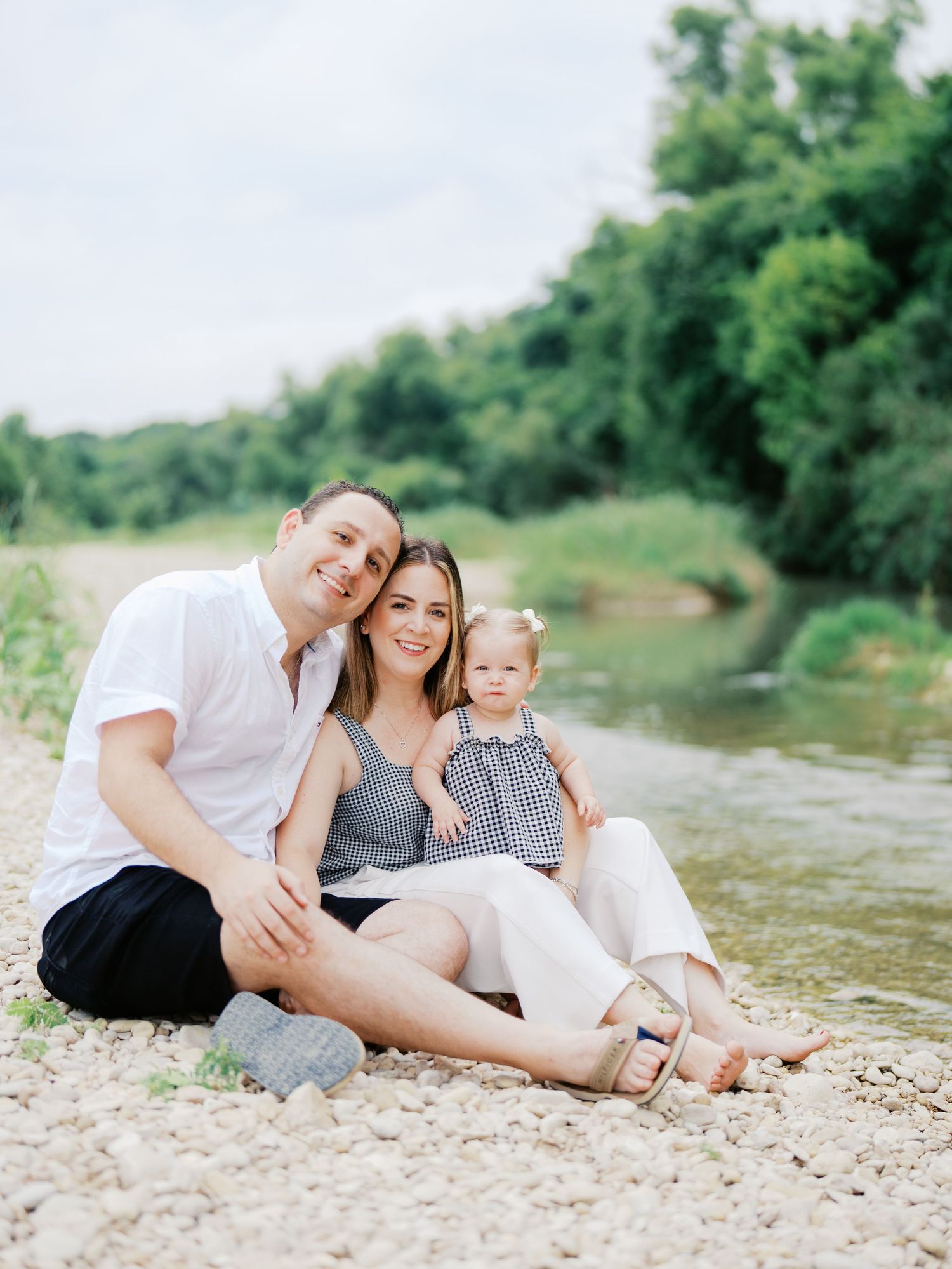 Family of three sitting by a creek in Bulverde, Texas during a one year family session.