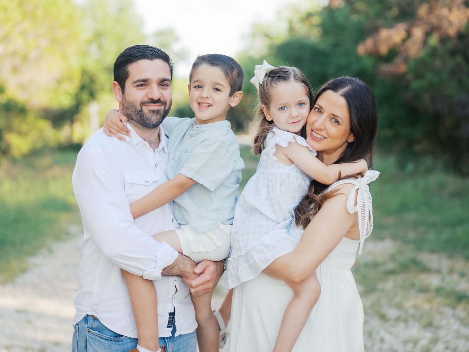 A family of four smiling for the camera during a maternity photoshoot outdoors in San Antonio, Texas