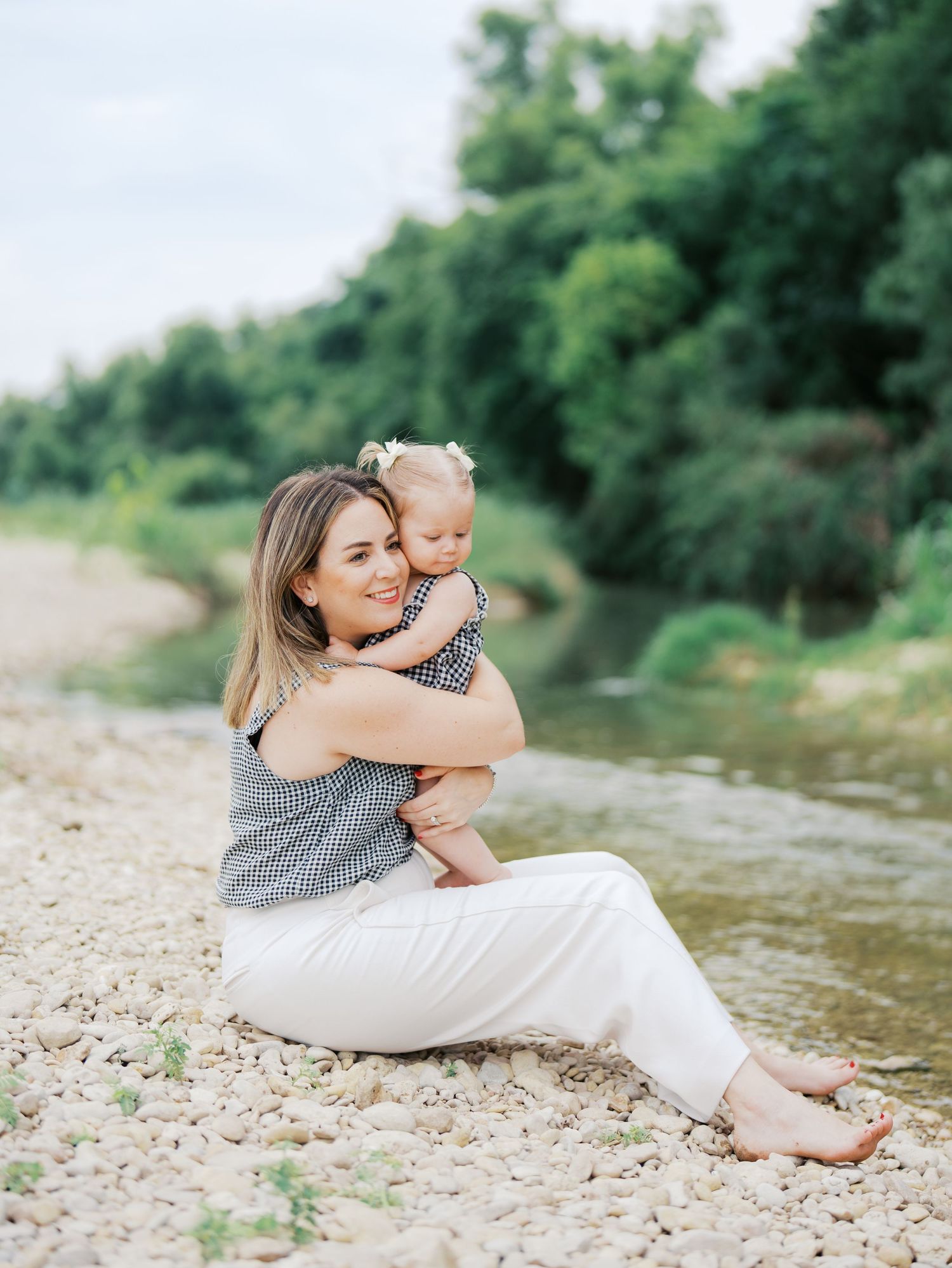Mom holding her one year old baby by a creek during an outdoor milestone session in Bulverde Texas