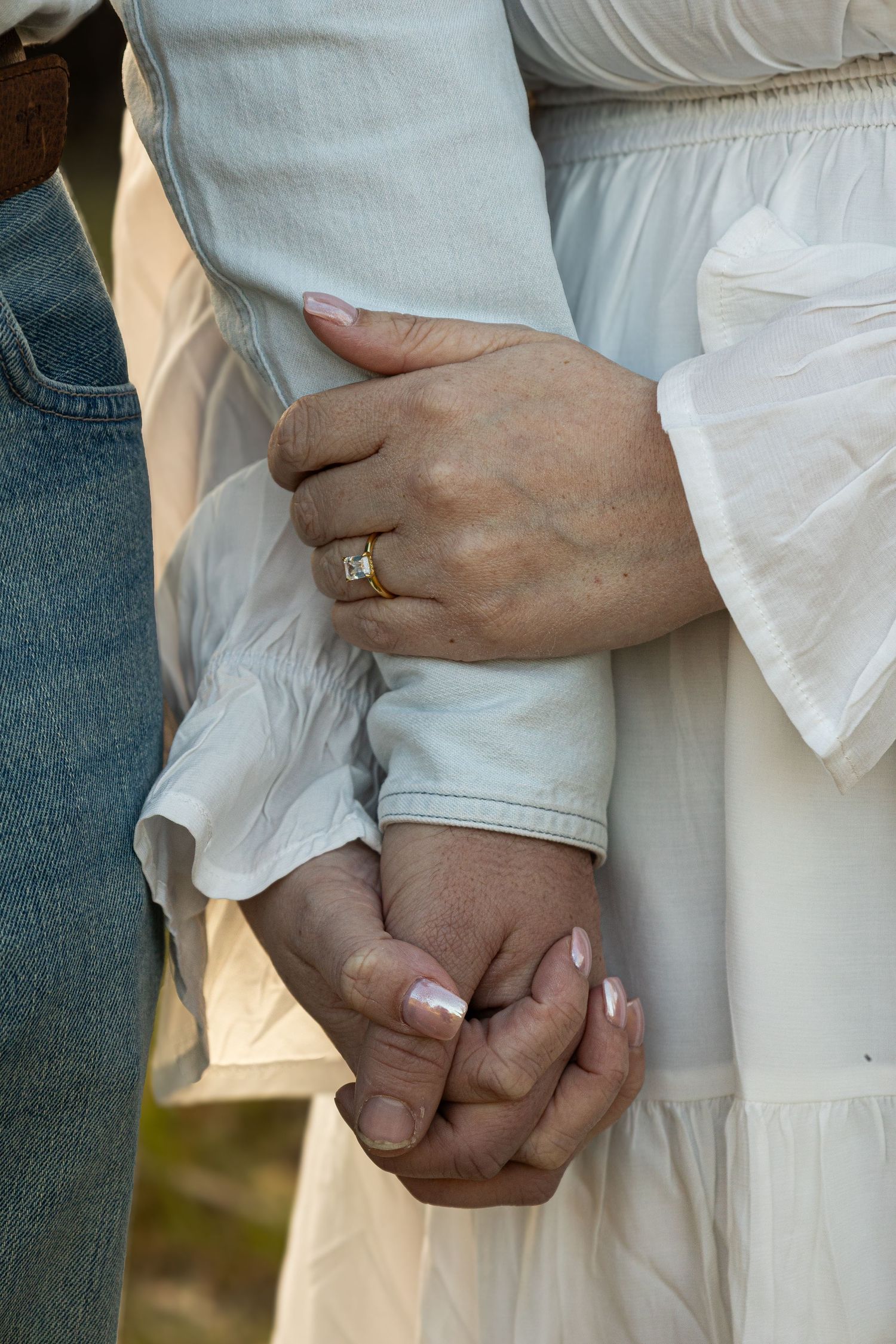 Close-up of intertwined hands showing engagement ring and white dress details.