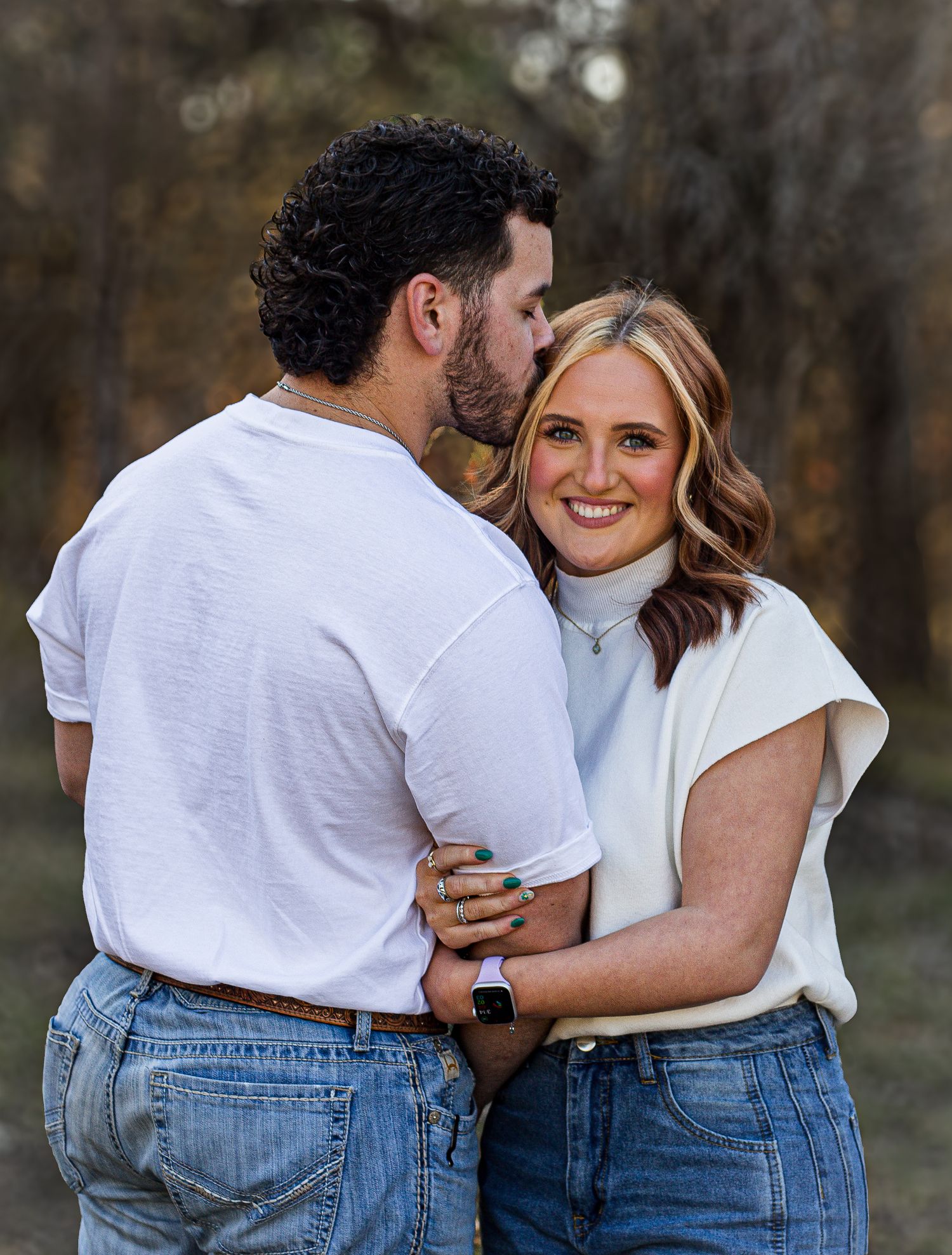A couple in matching white tops and jeans share an intimate moment outdoors.