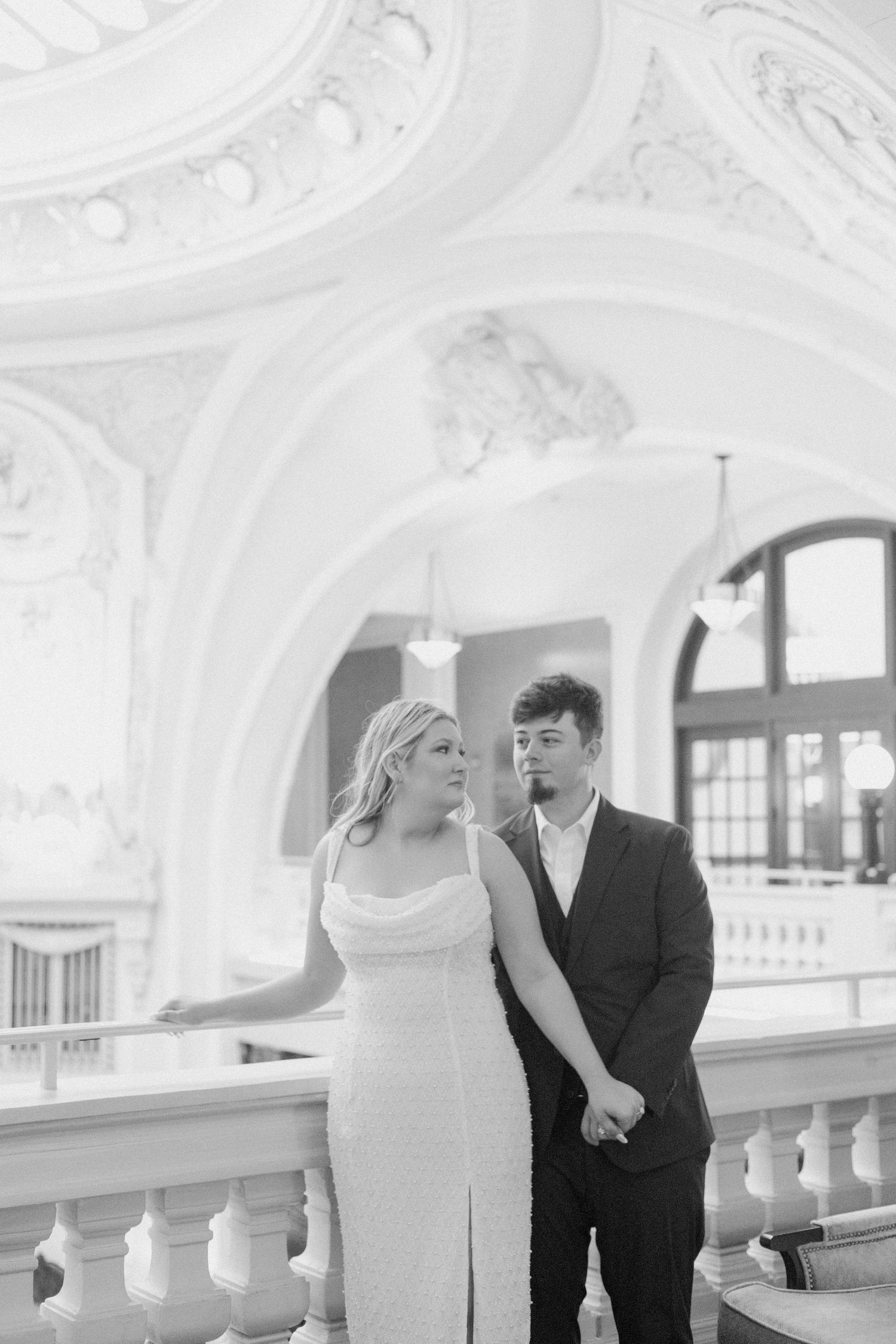 Elegant couple posing in formal wear inside historic building with ornate white architectural details.