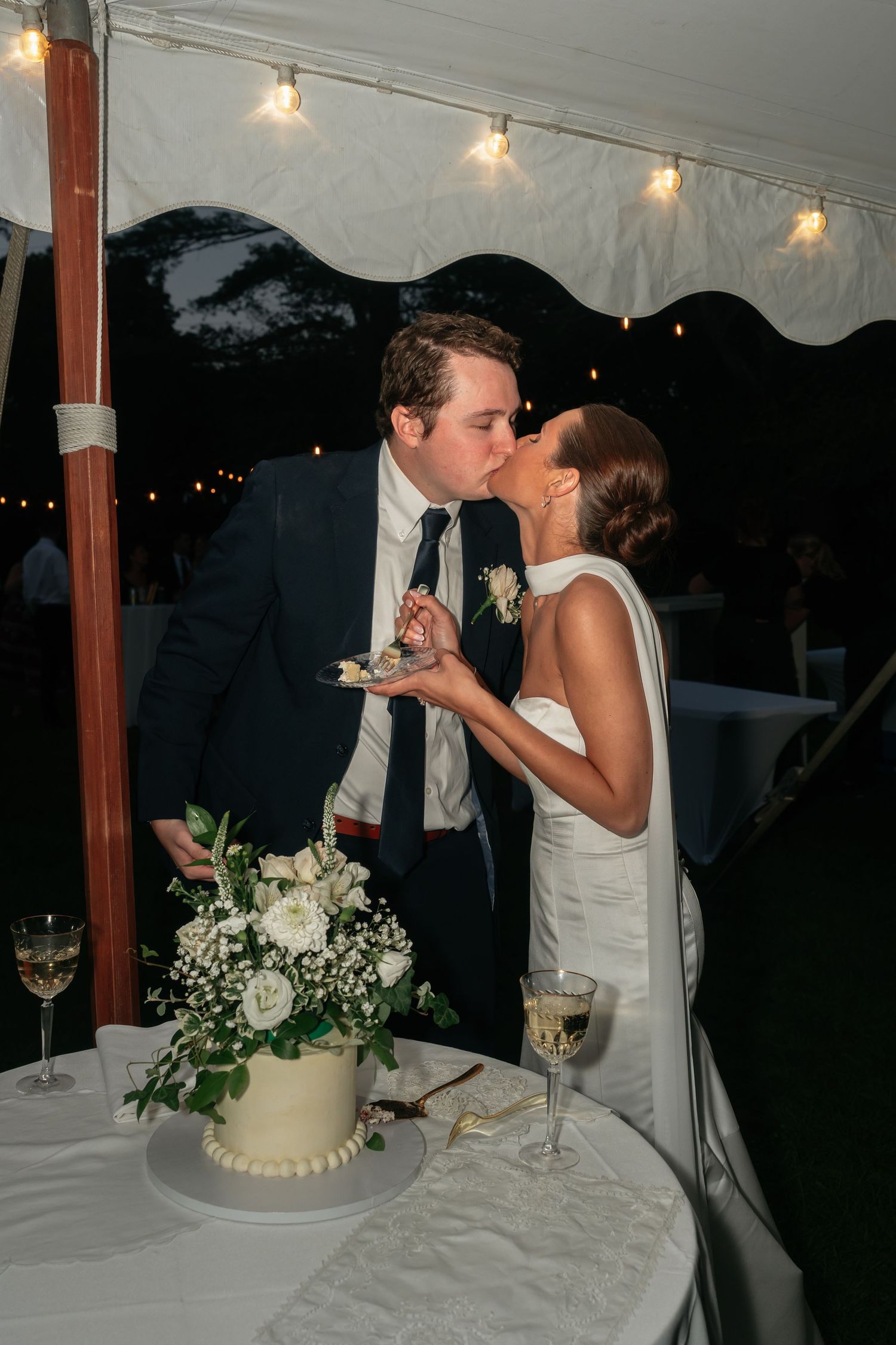 Wedding cake cutting ceremony under string lights at evening reception.