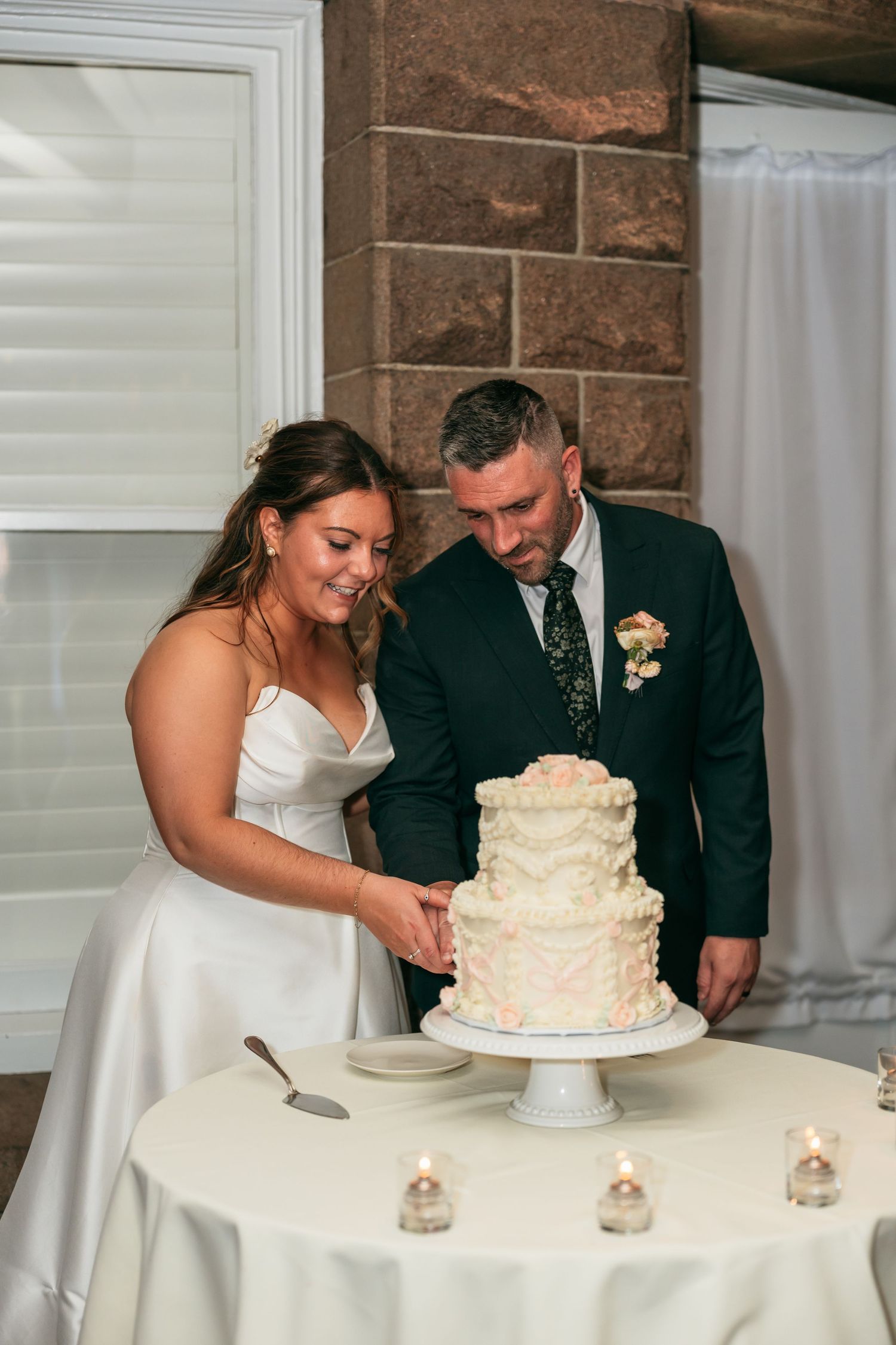 Couple cutting elegant white two-tier wedding cake at reception.