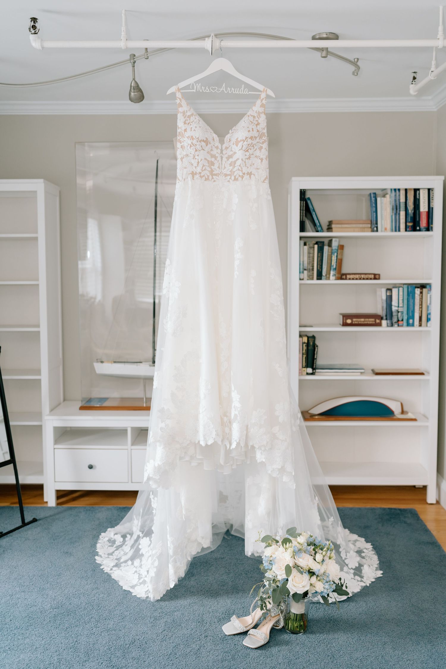 White lace wedding dress hanging in front of built-in bookshelves in preparation room.
