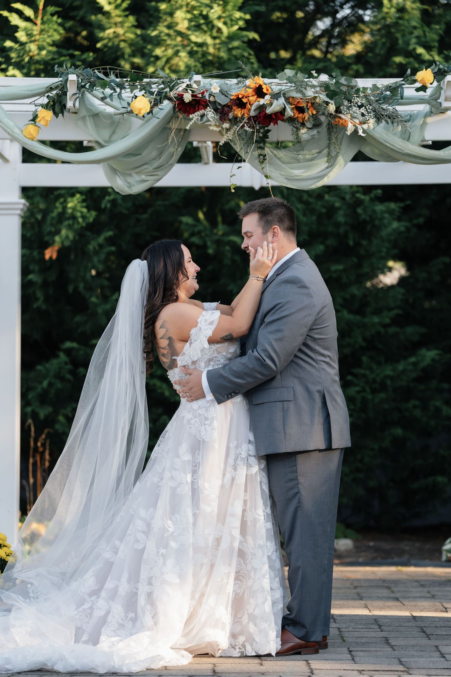 Romantic wedding ceremony moment under a white pergola with fall floral arrangements.