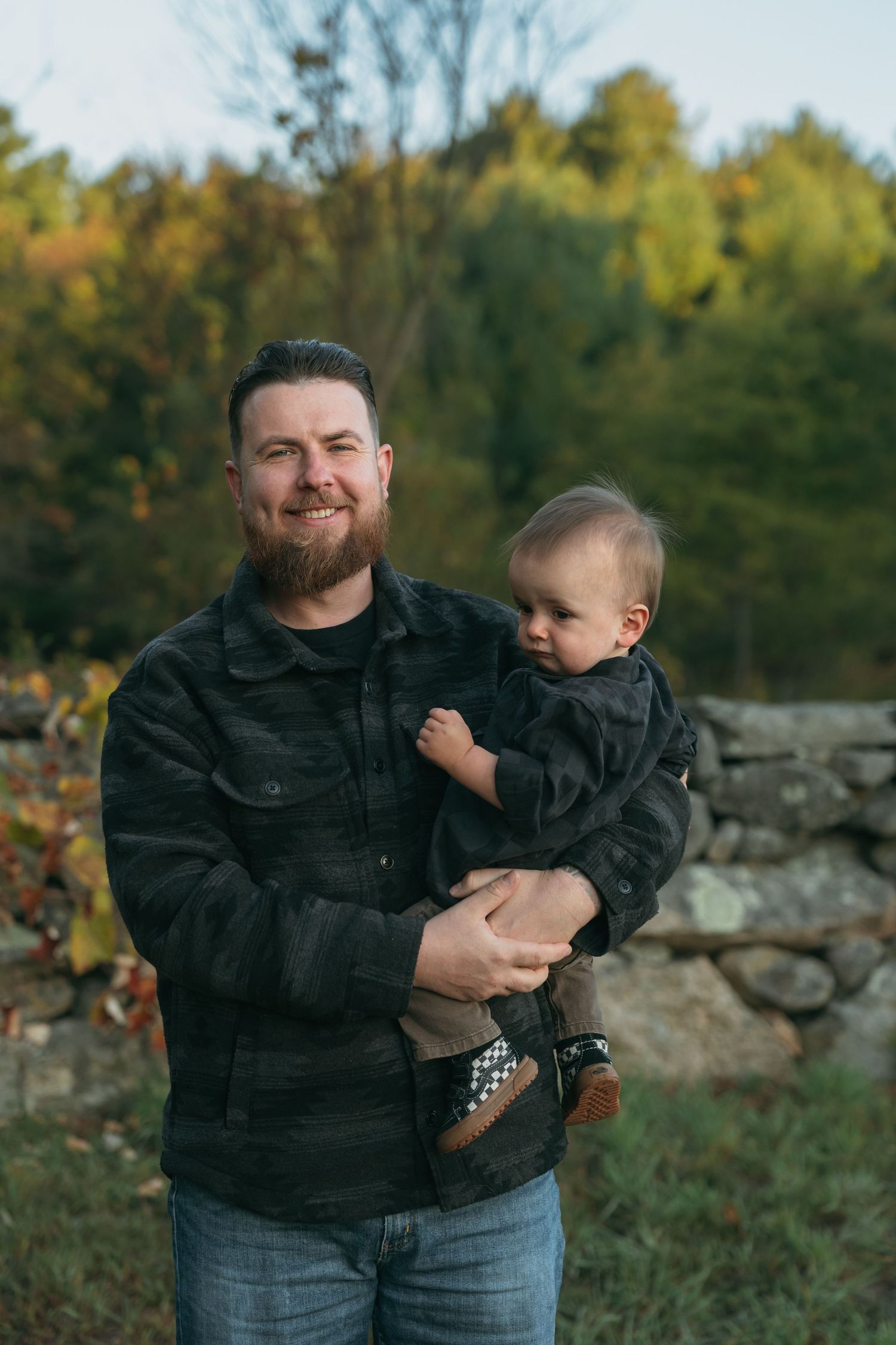 Joyful outdoor family moments captured against autumn trees and stone wall backdrop.