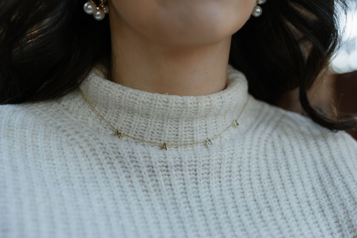 Close-up detail of white knit sweater and pearl earrings in natural lighting.
