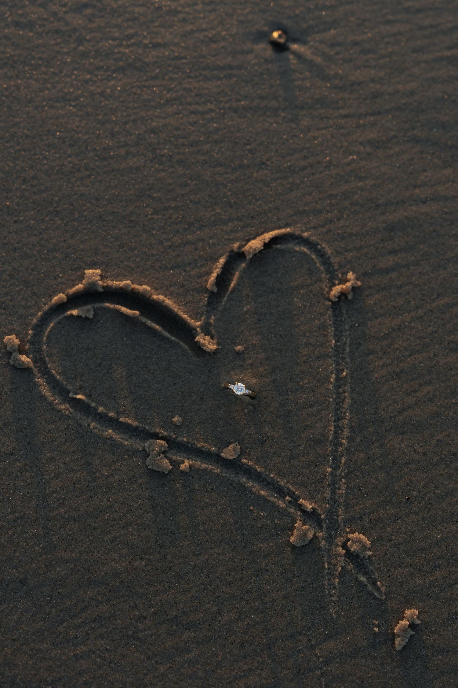 A heart shape drawn in sand on a dark beach at sunset.