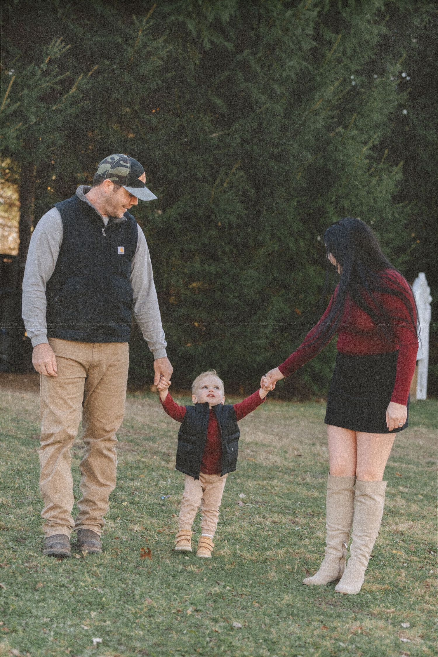 Family walking together through a grassy outdoor area wearing casual fall attire.