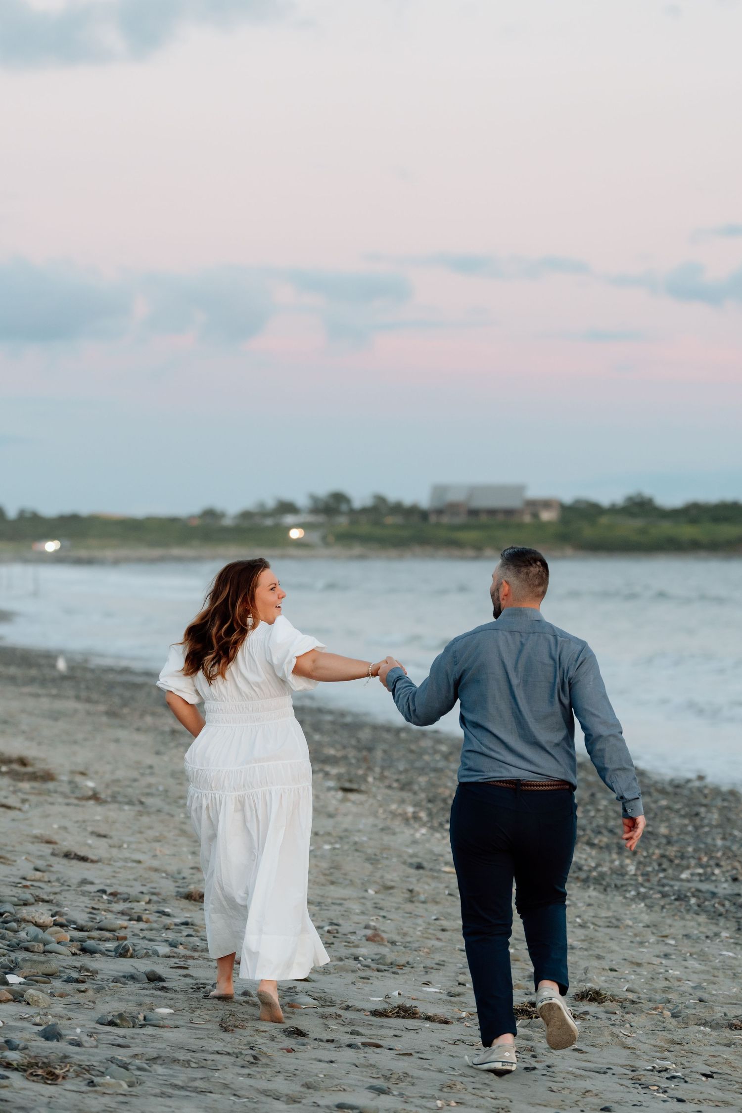 Couple playfully runs and dances together along a scenic beach shoreline at dusk.