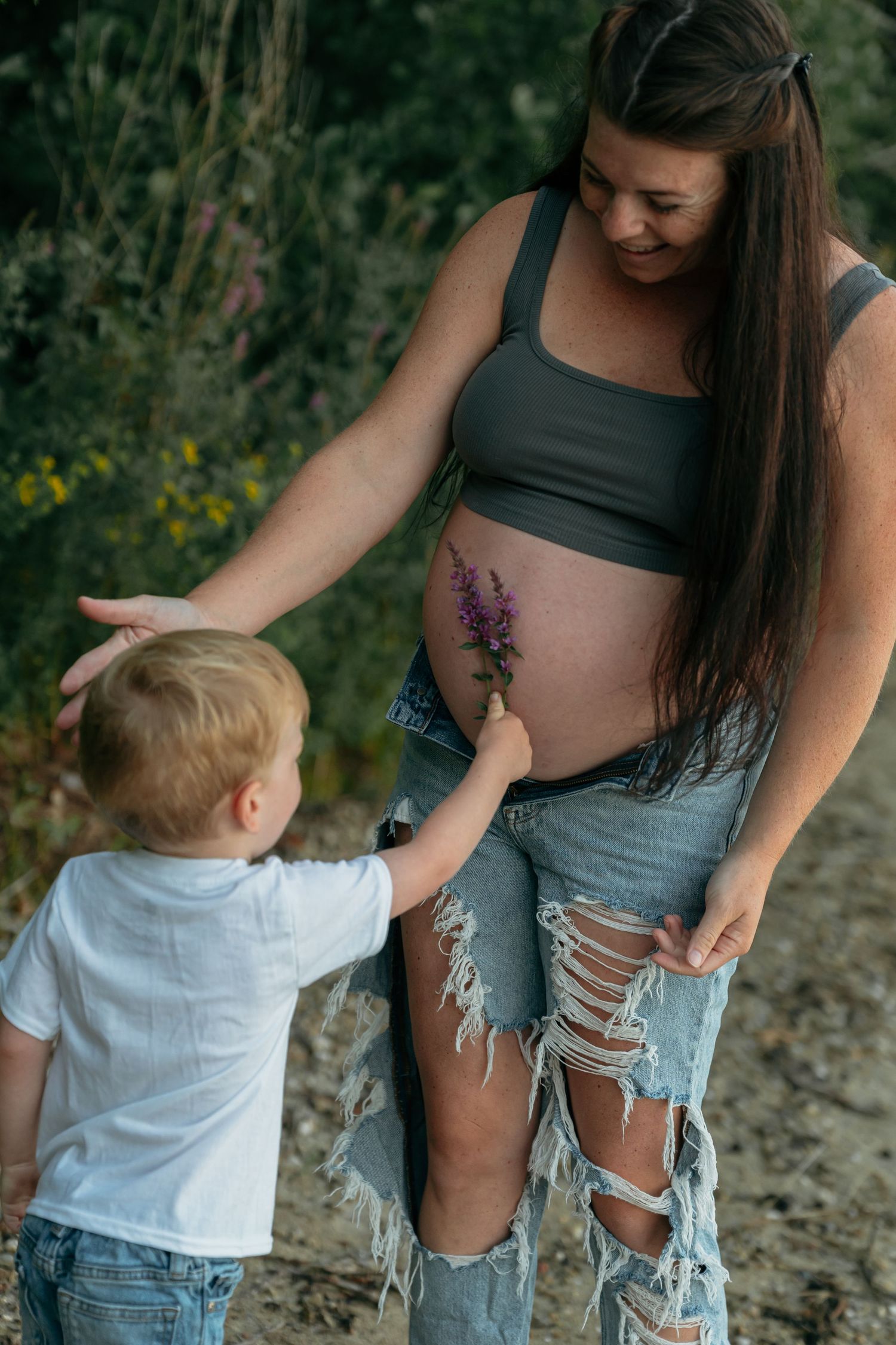Candid family moment captured along a rocky riverbank with trees in background.