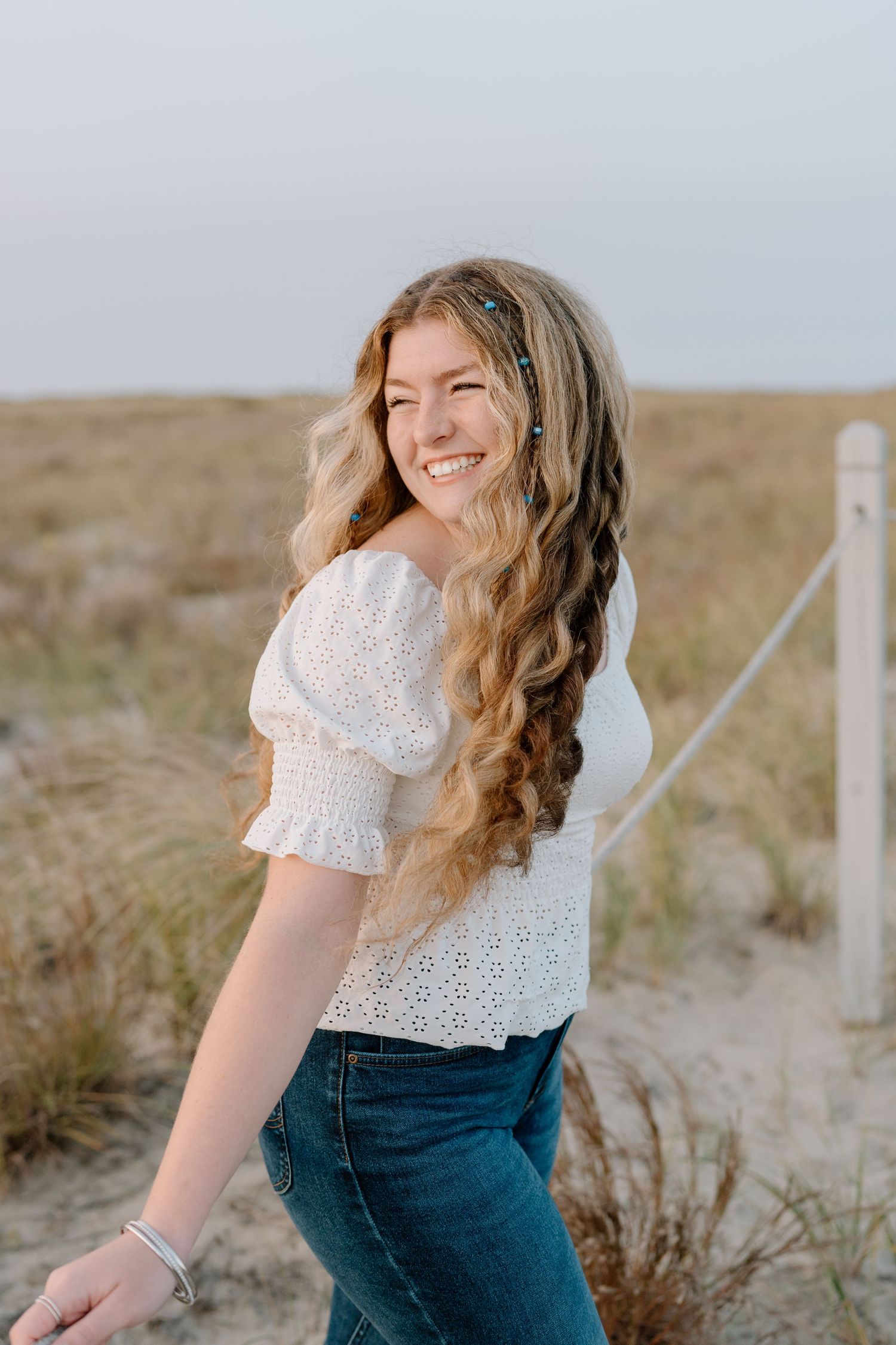 Candid outdoor photo showing white eyelet top and jeans while walking along a beach path.