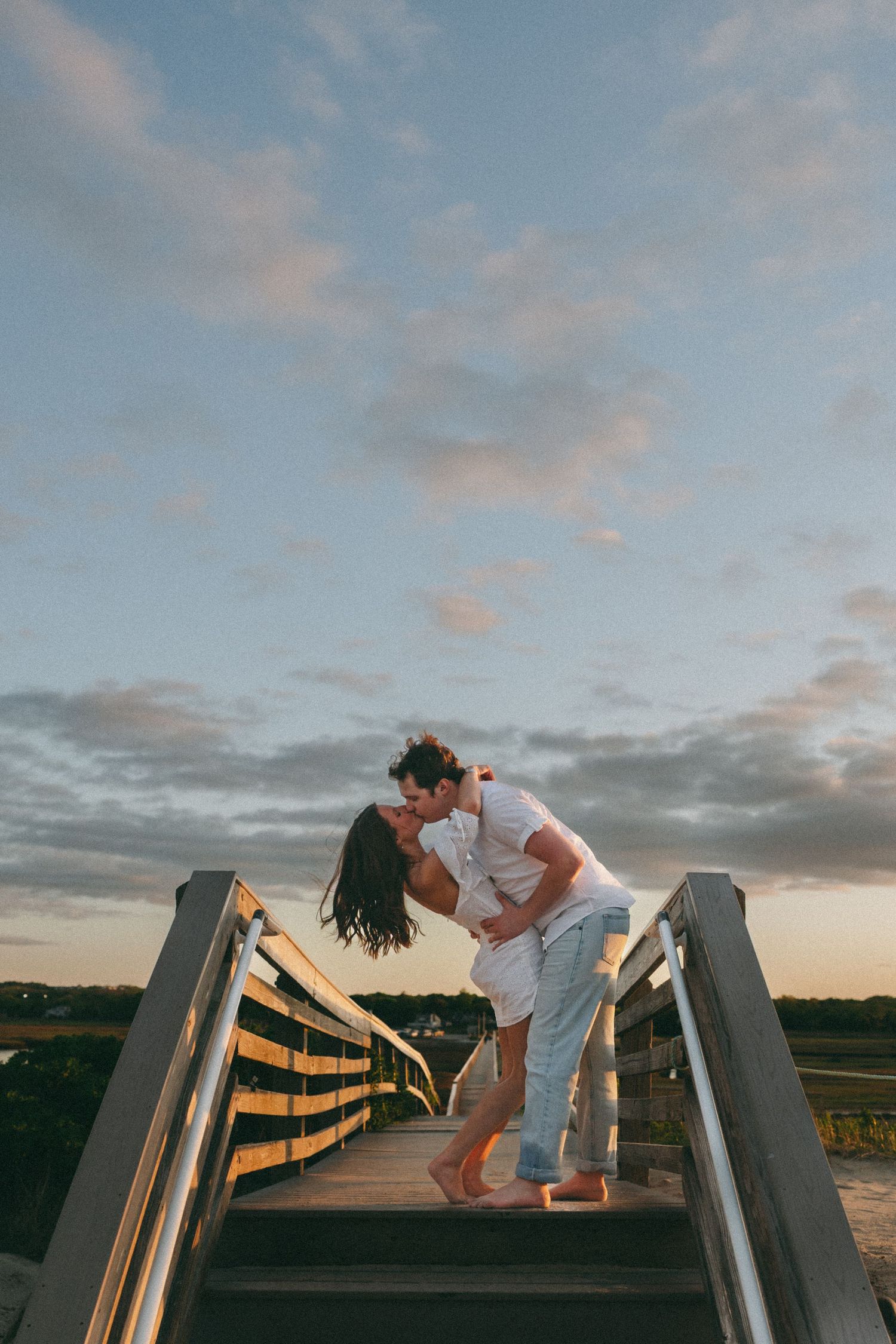 A couple dancing playfully on a wooden boardwalk at sunset.