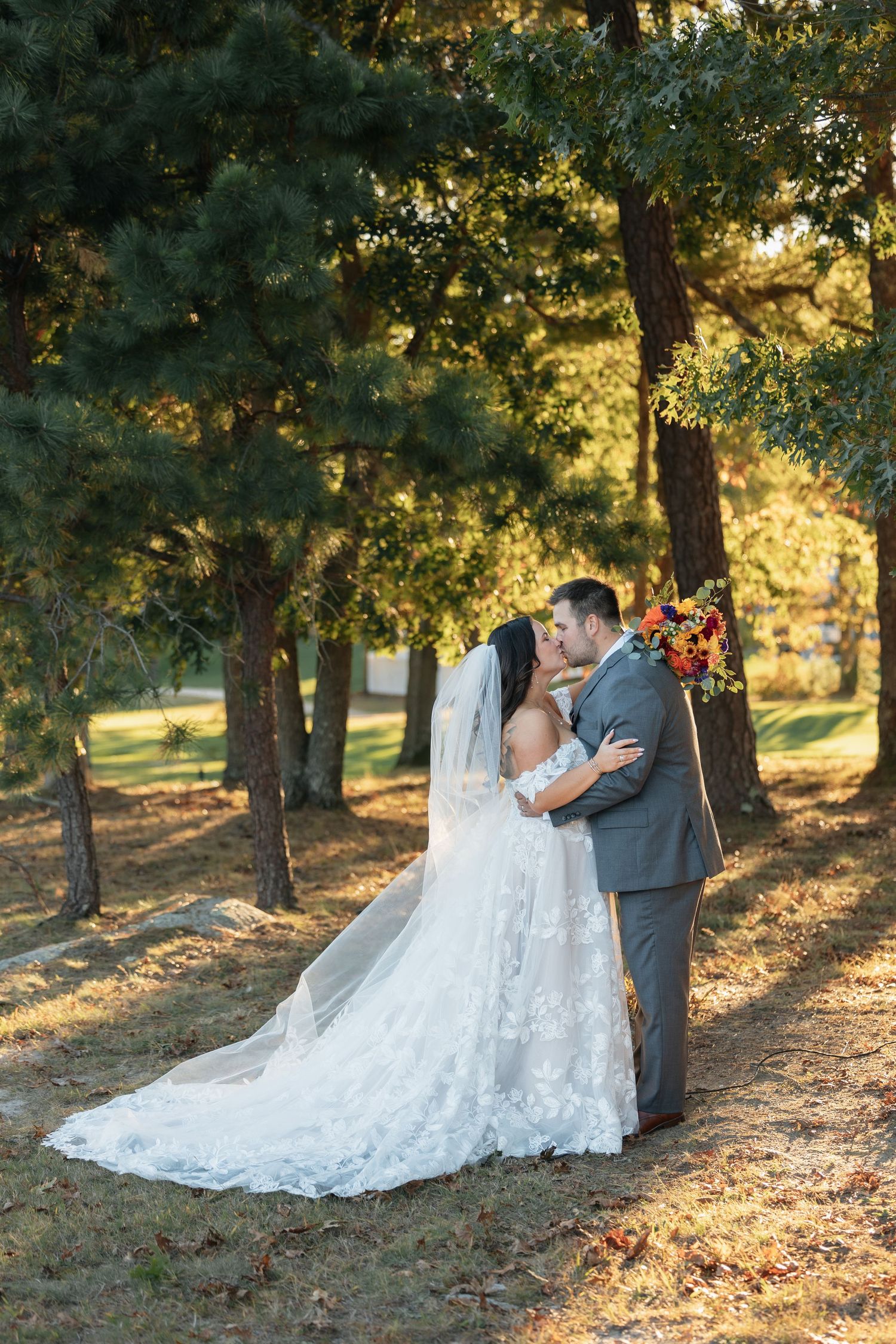 Wedding couple poses in golden autumn sunlight filtering through trees.