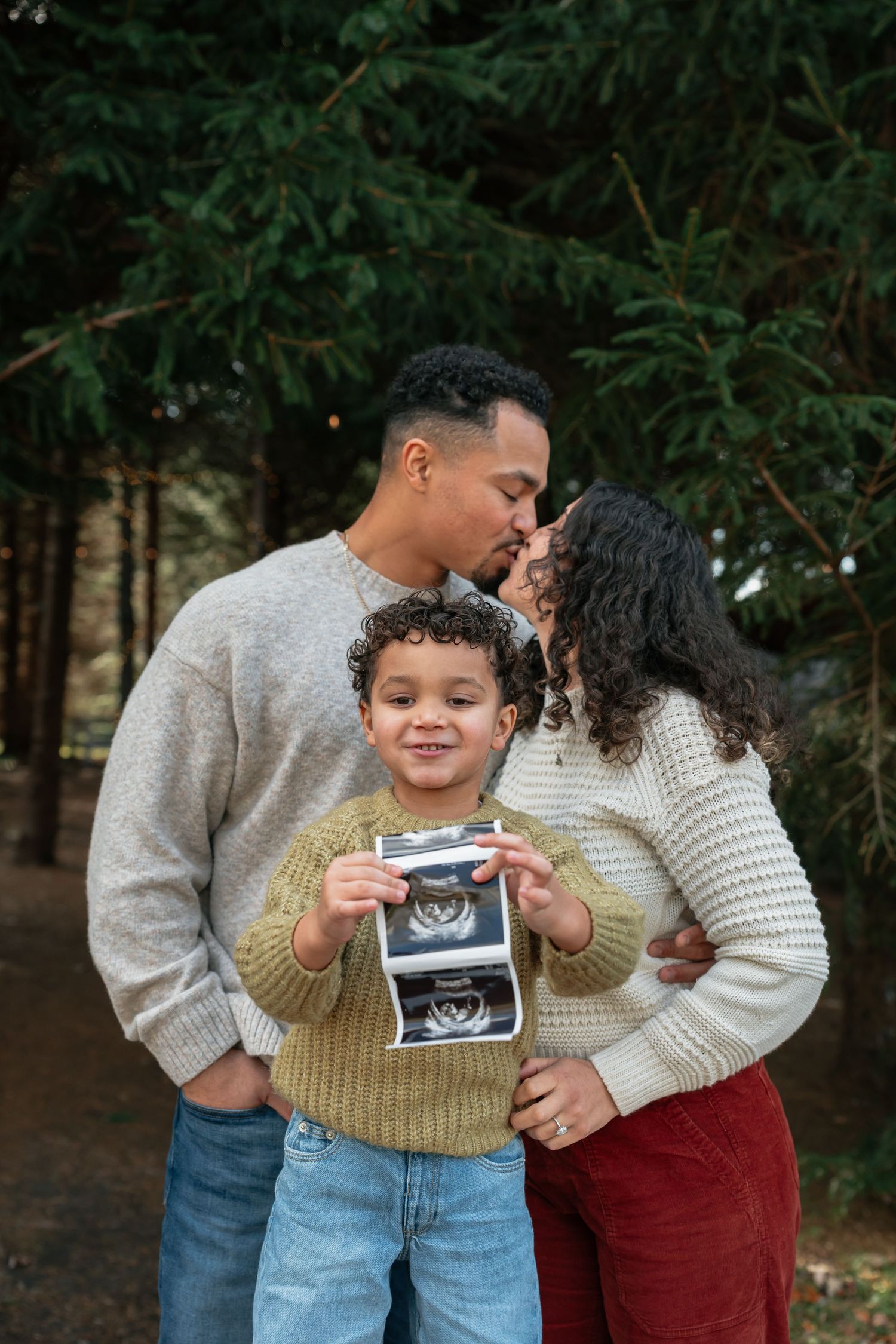 Family sharing a special moment while looking at an ultrasound photo in a forest setting.