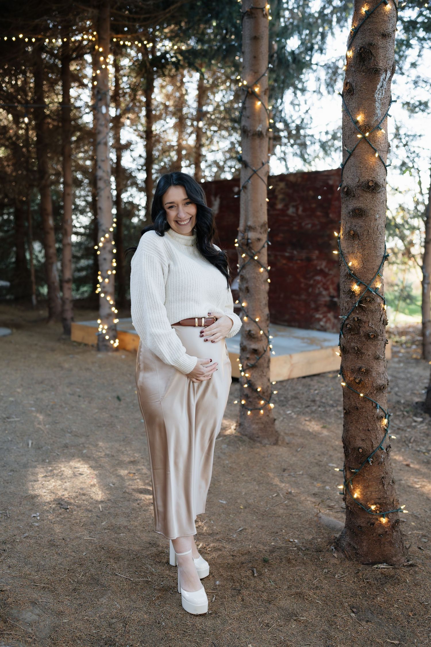 Maternity portraits in wooded area with twinkling lights and natural scenery.