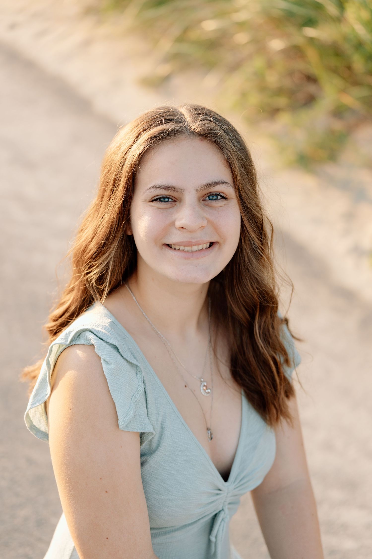 Portrait of someone in a mint green blouse smiling warmly against a natural outdoor background.