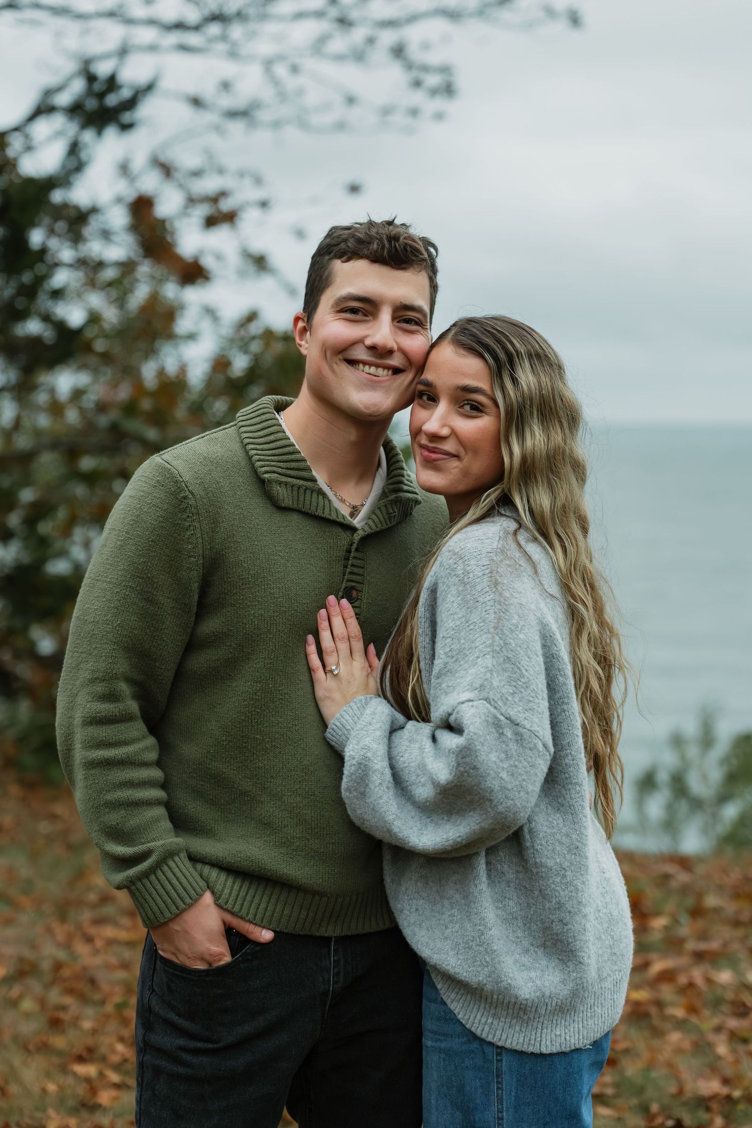A couple in cozy sweaters shares an intimate moment against a coastal backdrop.