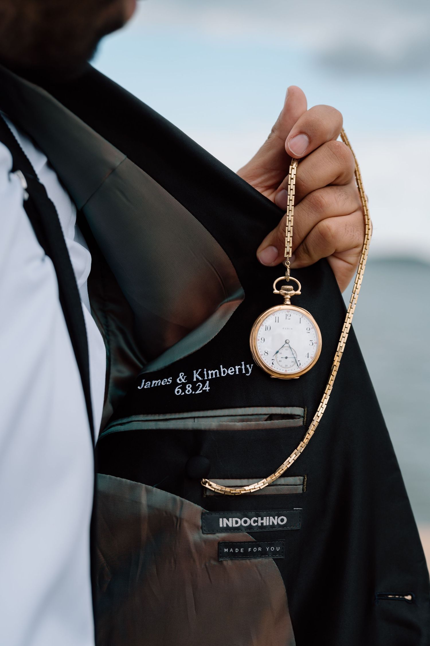 Vintage pocket watch with engraved names displayed against formal suit jacket.