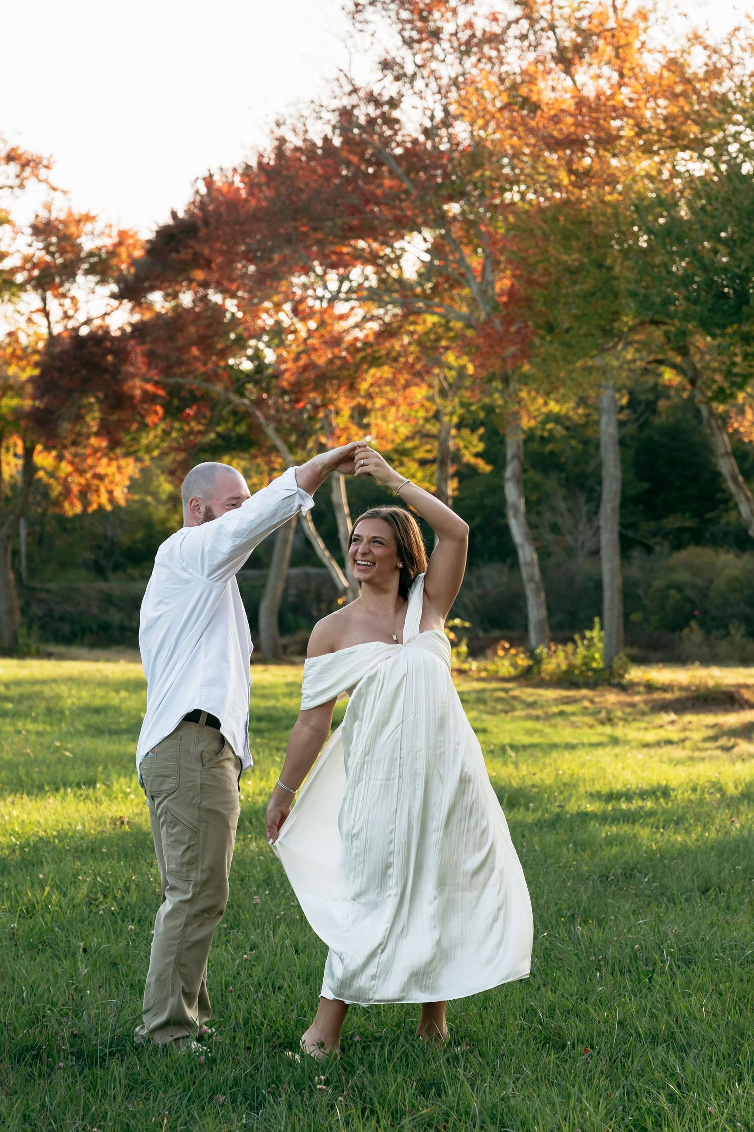 A couple twirls and dances together in a sunlit autumn field.