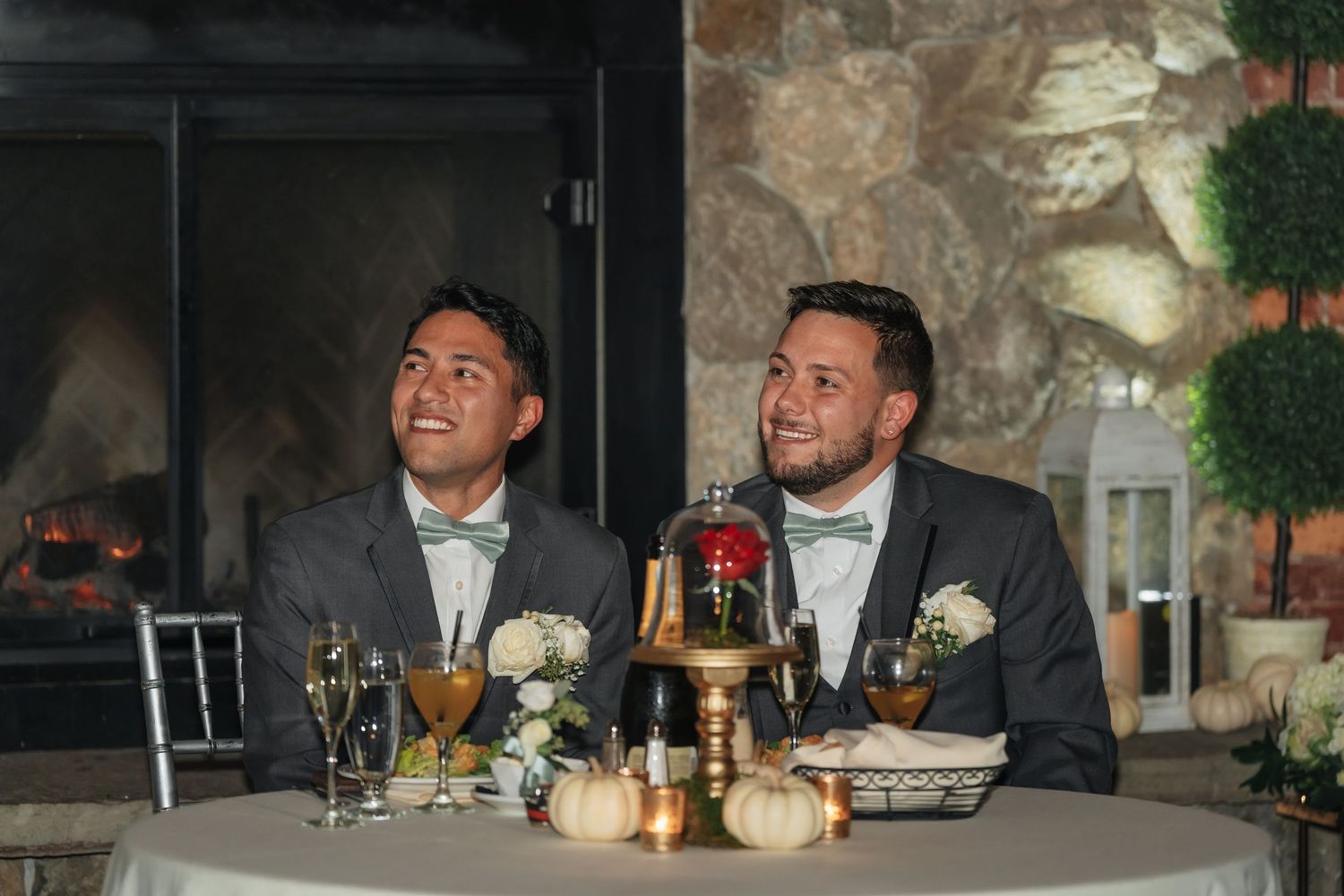 Wedding reception head table setup against stone wall backdrop with elegant place settings and decor.